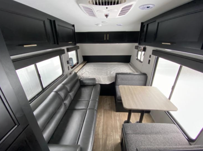 Spacious and modern RV rental interior showcasing a bed, black leather sofa, and dinette with wood-look flooring.. Forest River Cherokee Wolf Pup 2021