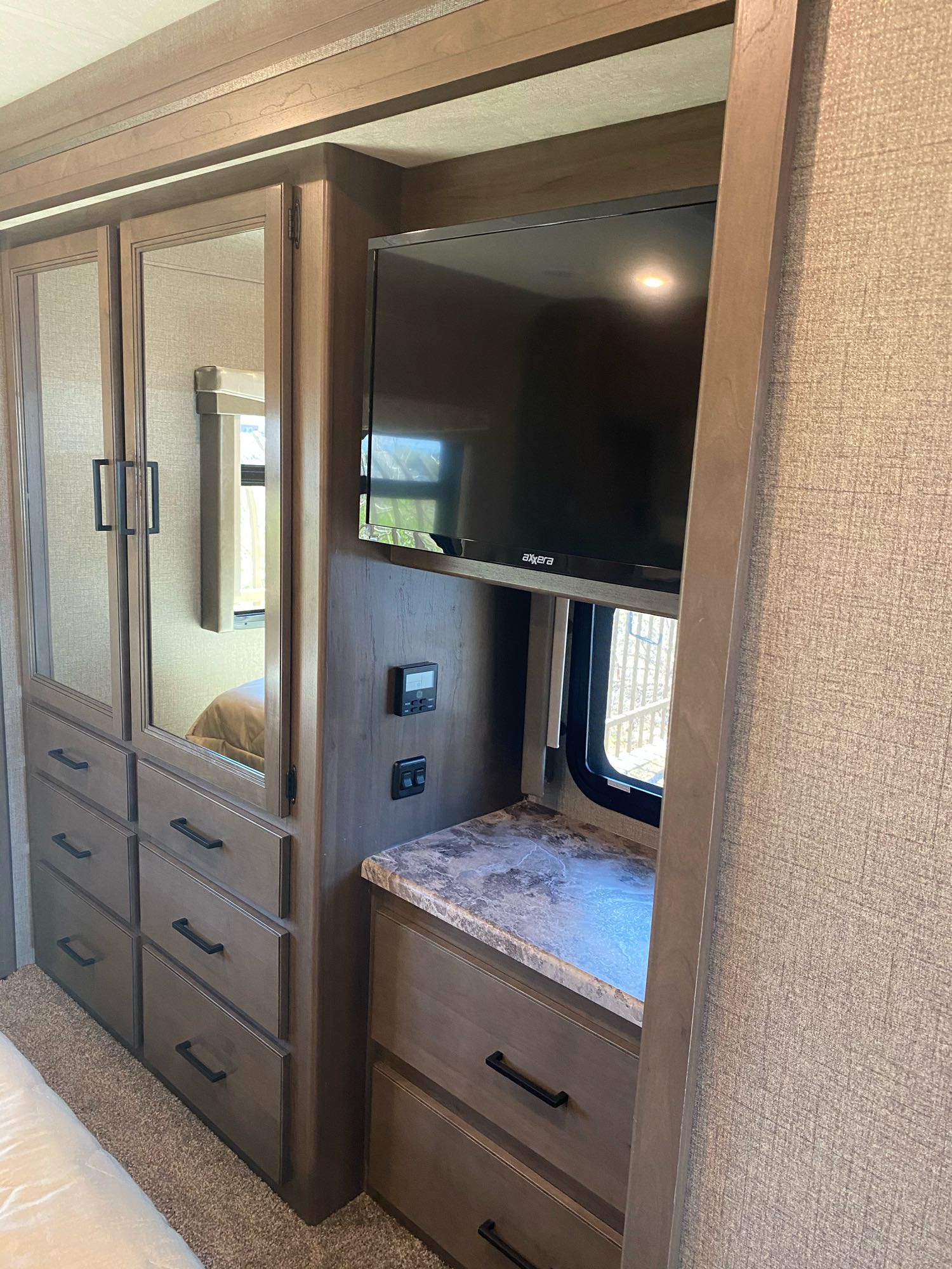 RV rental bedroom interior with mirrored closet, multiple drawers, wall-mounted TV, and window detail.. Thor A.C.E. 2021