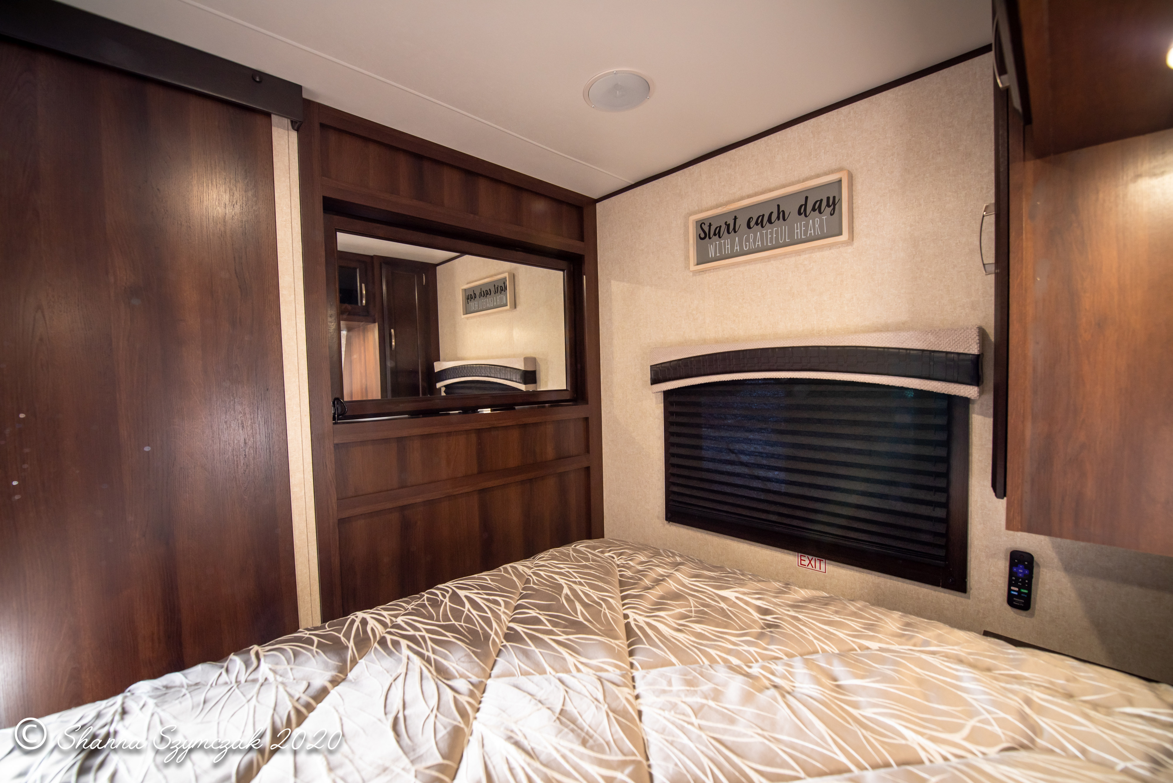 Cozy RV rental bedroom featuring dark wood cabinetry, a comfortable bed, window with blinds, and decorative sign.. Jayco Bunkhouse 2020