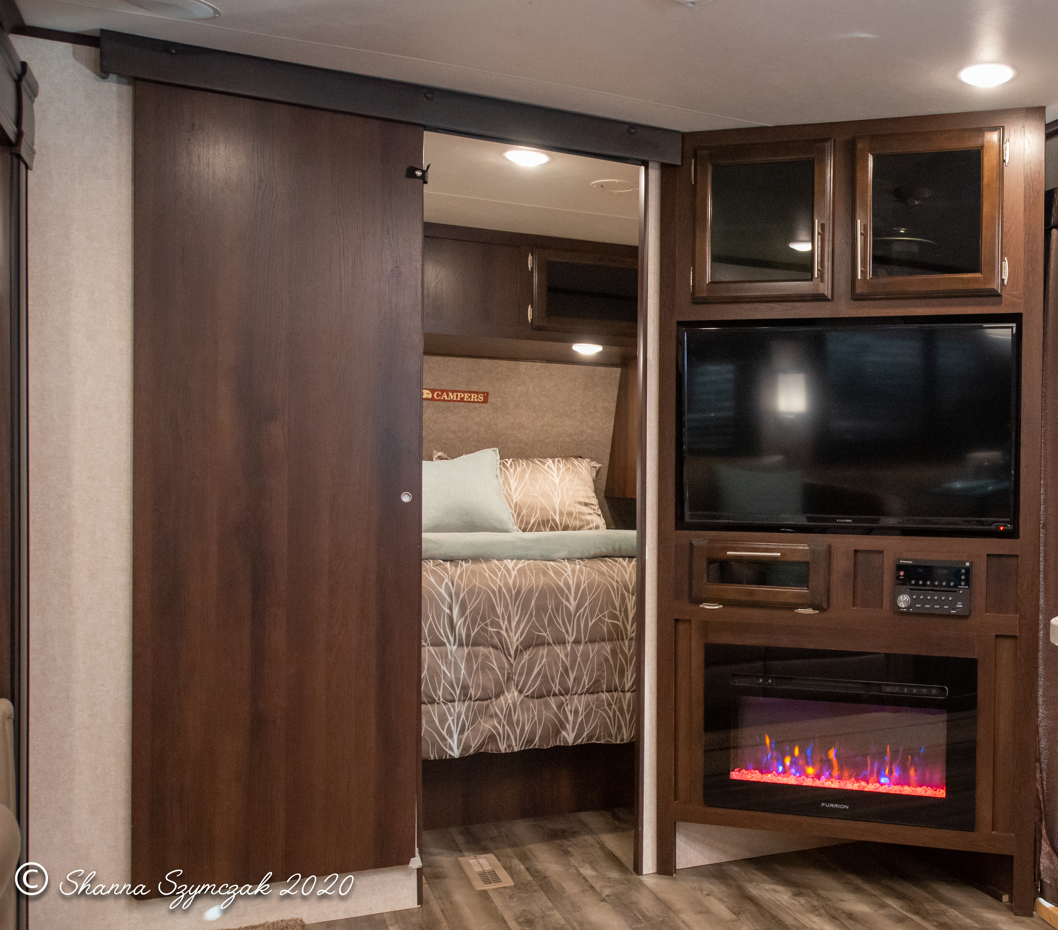 An rv rental interior featuring a bedroom accessed by a sliding door, a large TV, and an electric fireplace.. Jayco Jay Flight 2020