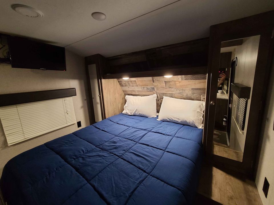This cozy RV rental bedroom features a comfy blue bed, mounted TV, & rustic headboard for your travels.. Dutchmen Aspen Trail 2019