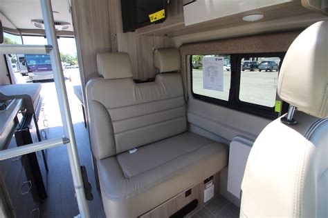 Modern RV rental camper van interior: light-colored dinette bench, a ladder, and large windows revealing the exterior.. Thor Sequence 2021