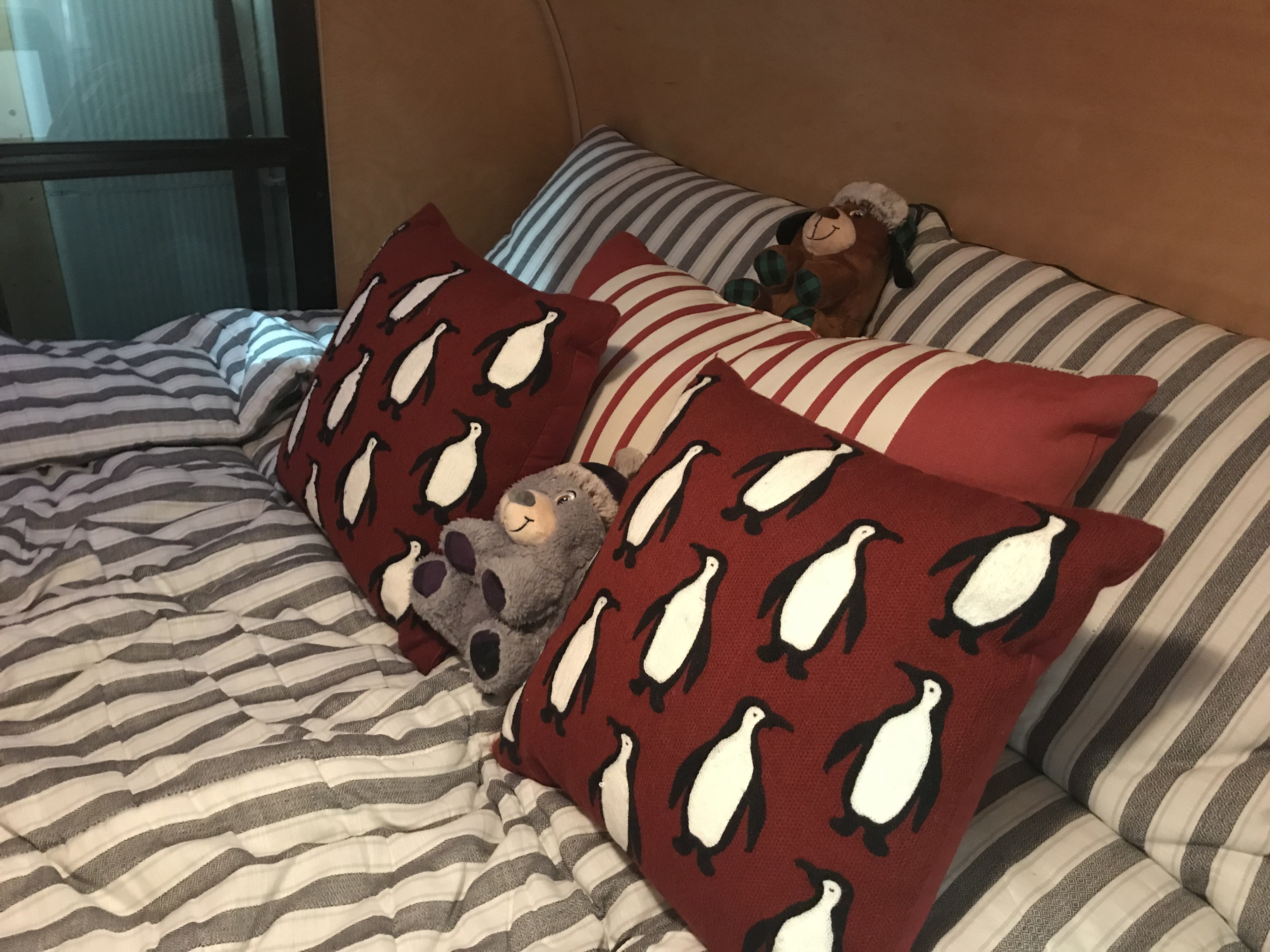An RV rental's comfy bed features striped bedding, red penguin pillows, and two soft stuffed animals.. Little Guy 5x8 Silver Shadow 2008