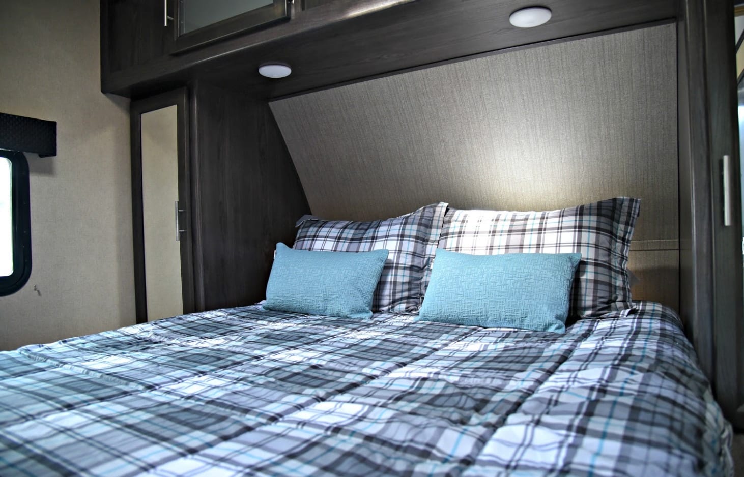 Cozy RV rental bedroom with plaid bedding and light blue pillows. Features overhead cabinets and integrated lighting.. Dutchmen Kodiak 2020