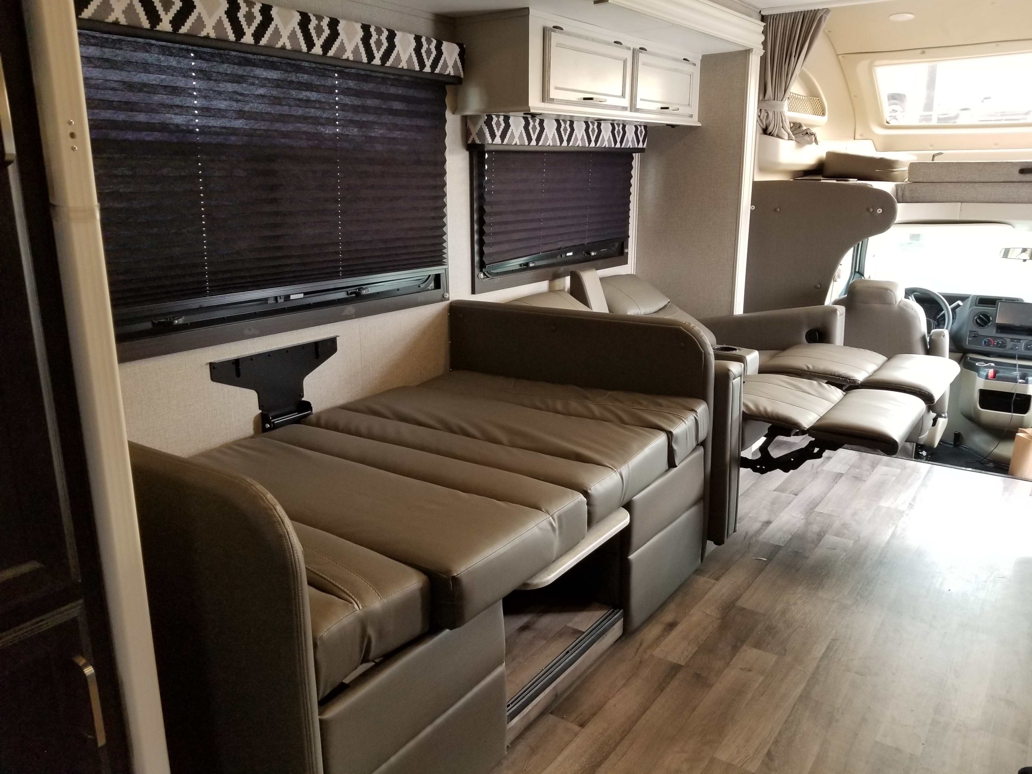 Spacious RV rental interior with convertible seating unfolded into a bed, blinds, cabinets, and wood flooring.. Entegra Coach Other 2021