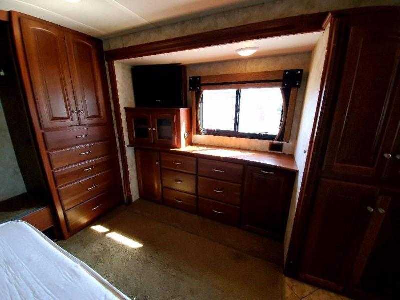 RV rental bedroom with rich wooden cabinetry, built-in storage, bed, window, and TV. A cozy space for your next road trip.. Winnebago Adventurer 2011