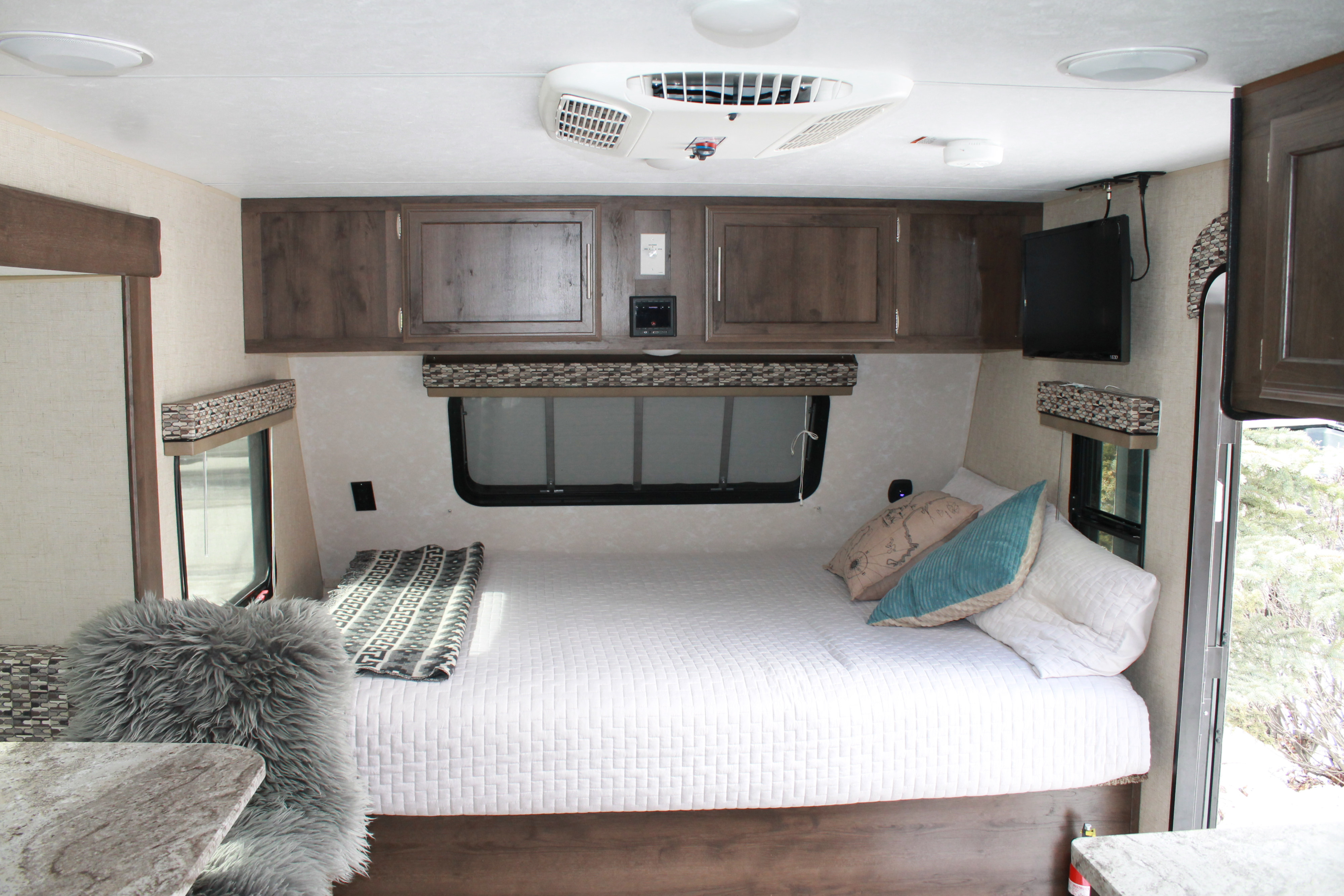 Inside a comfortable RV rental: A bedroom with white bedding, pillows, overhead cabinets, and a compact living space.. K-Z Manufacturing Spree 2017
