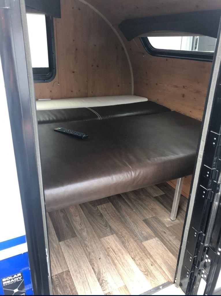 Cozy RV rental interior: brown cushioned bed, wood-paneled walls, and windows. Ideal for road trip comfort.. Sunset Park RV SunRay 2019