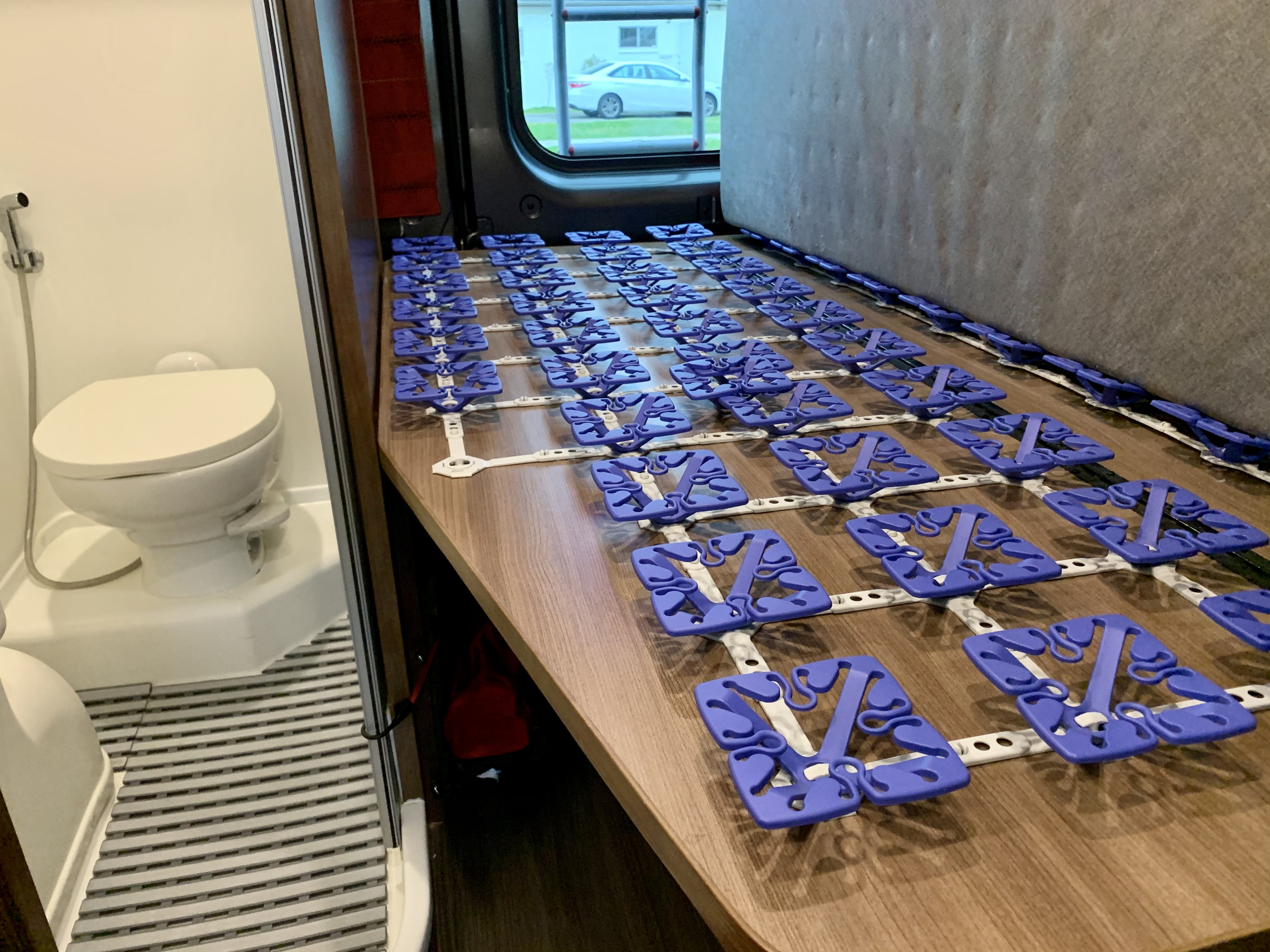 RV rental interior: compact bathroom with toilet and a bed base featuring purple mattress suspension modules.. Winnebago Travato 2018