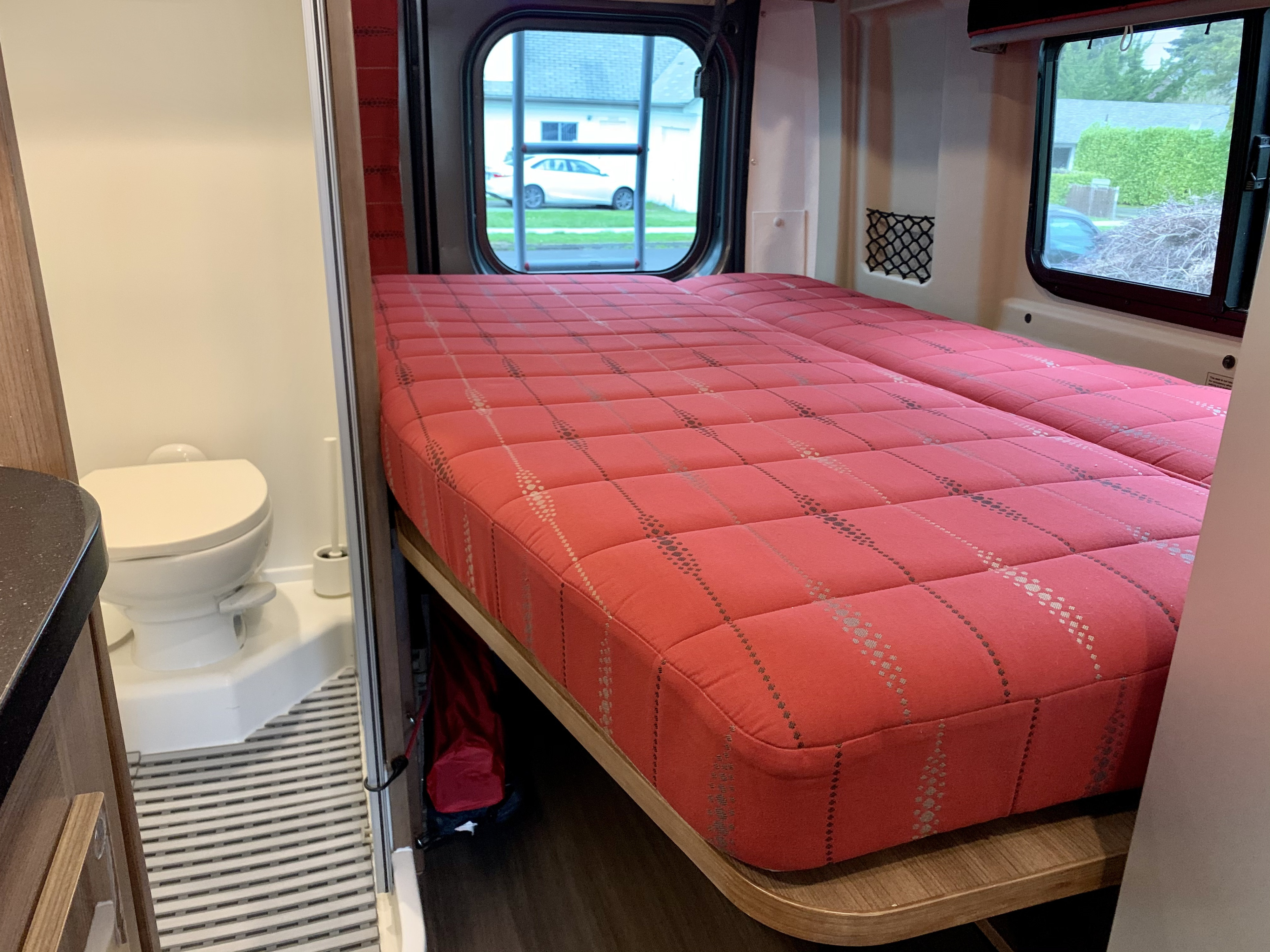 RV rental bedroom and bathroom. Features a large red bed, built-in toilet, and window views.. Winnebago Travato 2018