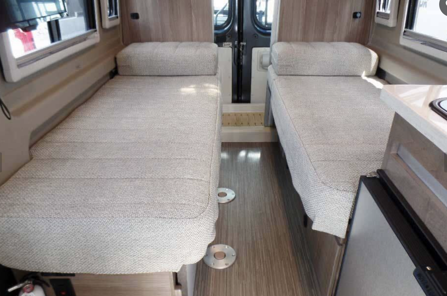 Inside an RV rental: view of twin upholstered beds with a central aisle, wood flooring, and a compact kitchen.. Winnebago Travato 2019