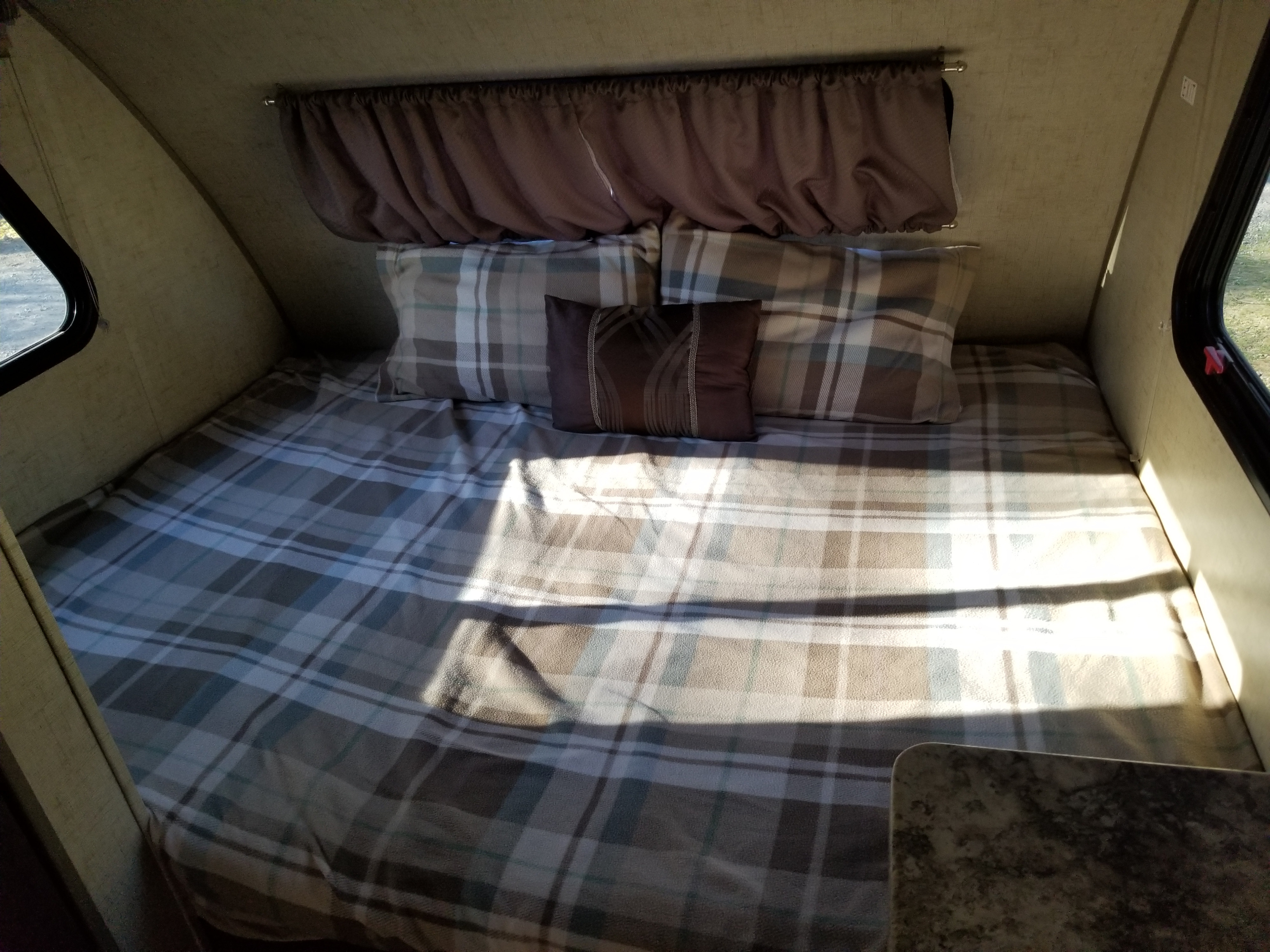 Inside a compact RV rental: a comfortable plaid bed with pillows and windows, ideal for campers.. Forest River R-Pod 2016