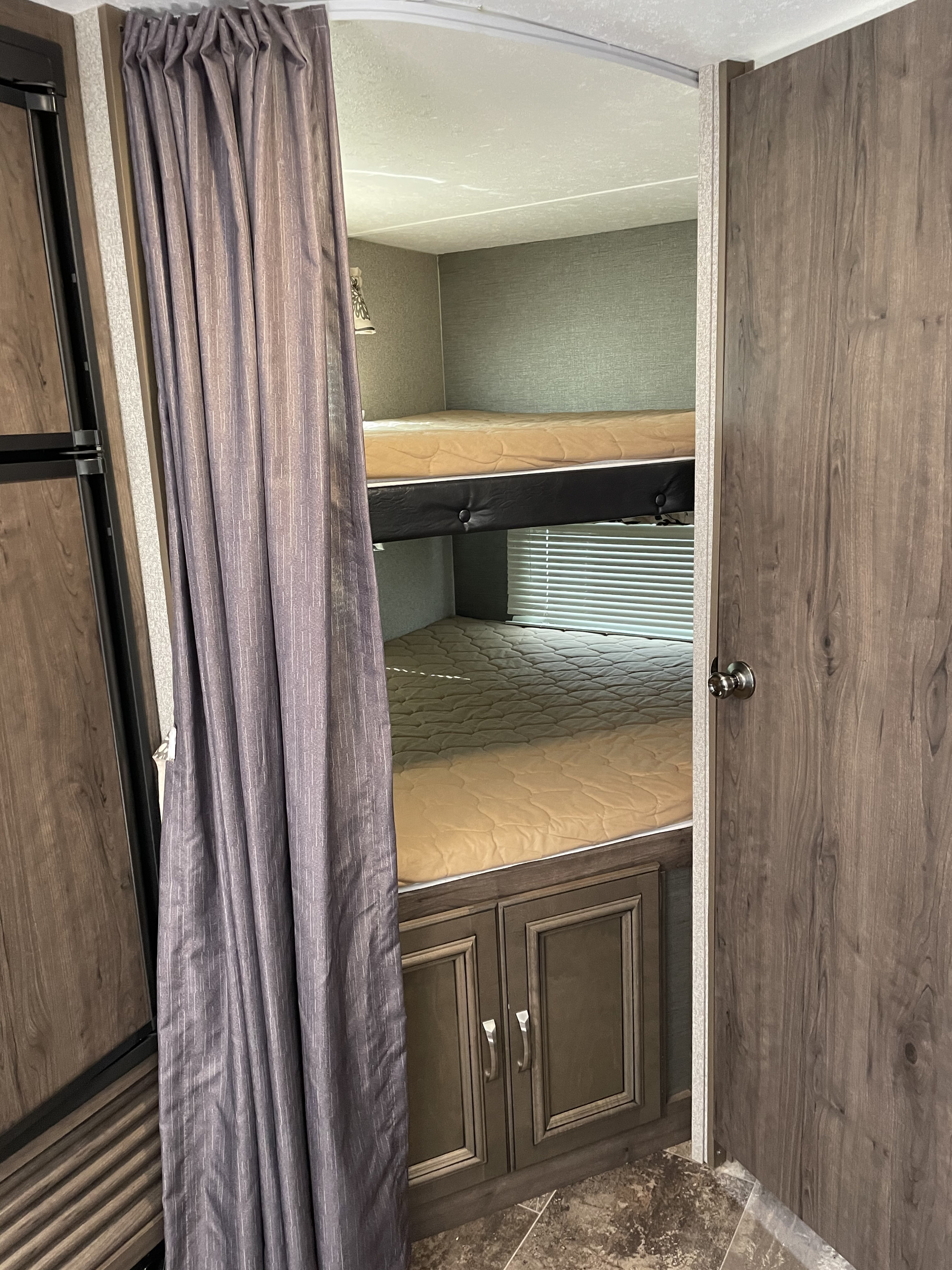 RV rental interior: two bunk beds with tan mattresses, a privacy curtain, storage cabinet, and window blinds.. Keystone Passport 2400BHWE 2018
