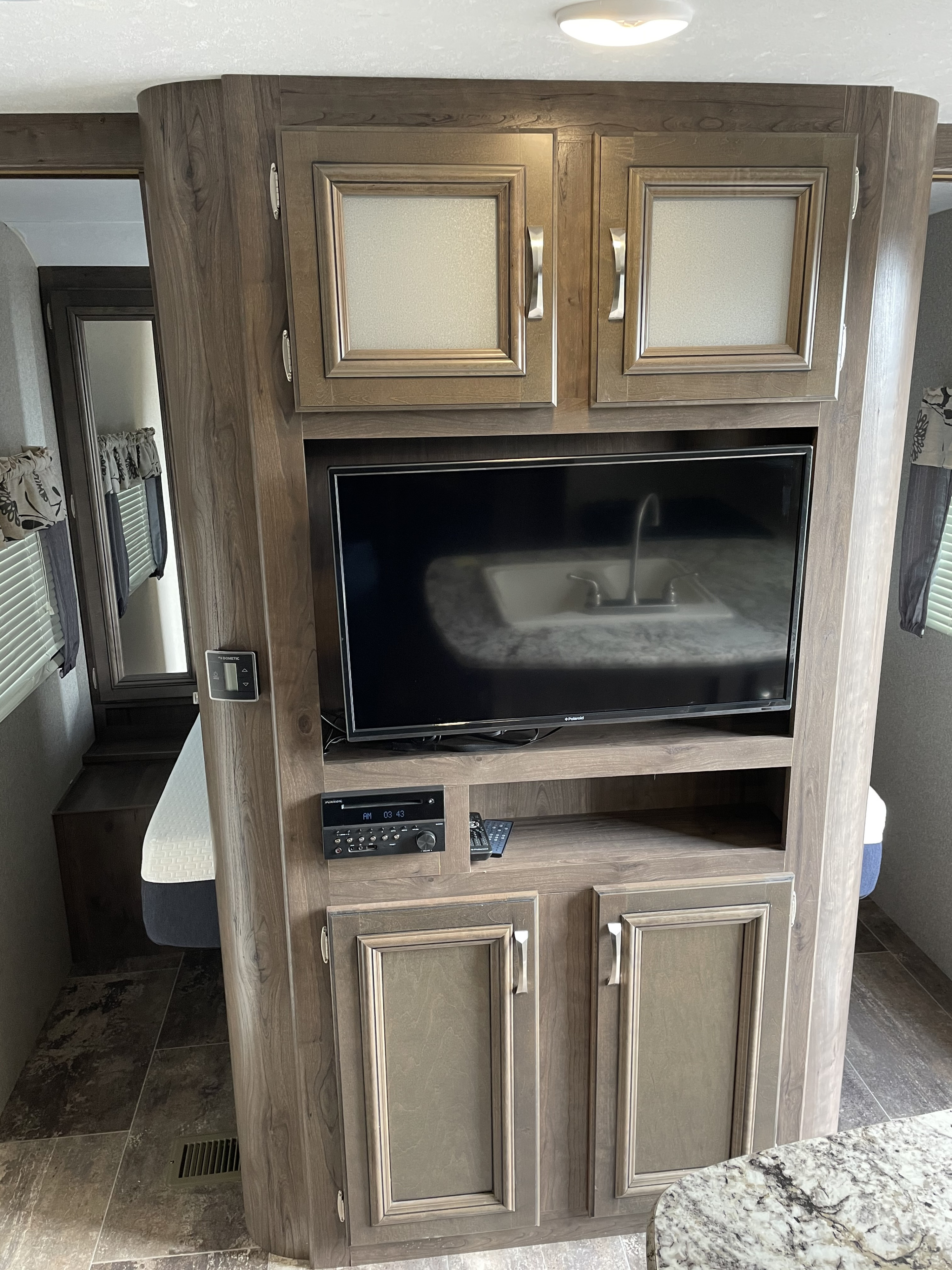 Modern RV rental interior featuring a TV, stereo, ample storage cabinets, and a glimpse of the bedroom area.. Keystone Passport 2400BHWE 2018