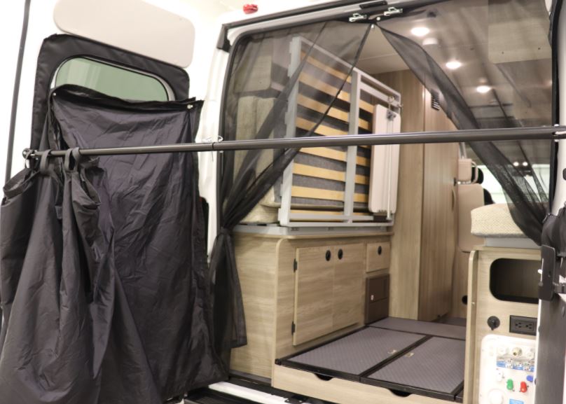 RV rental camper van interior showing a foldable bed, storage, rear bug net, and outdoor privacy screen.. Winnebago Solis 2021