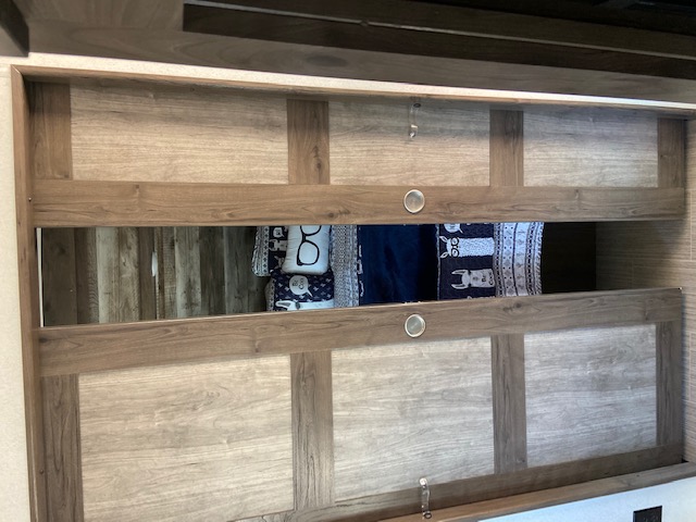 Inside an RV rental, this cozy bunk features warm wooden panels, a comfy bed with soft blankets and charming patterns.. Keystone RV Passport 2021