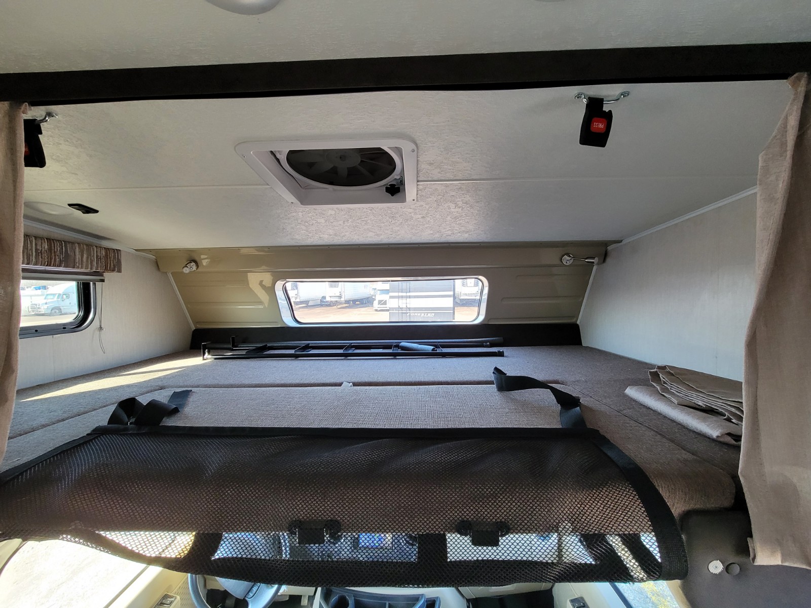 RV rental interior showing the large cab-over bunk, mesh safety net, ceiling fan, and side windows.. Coachmen Leprechaun 2021