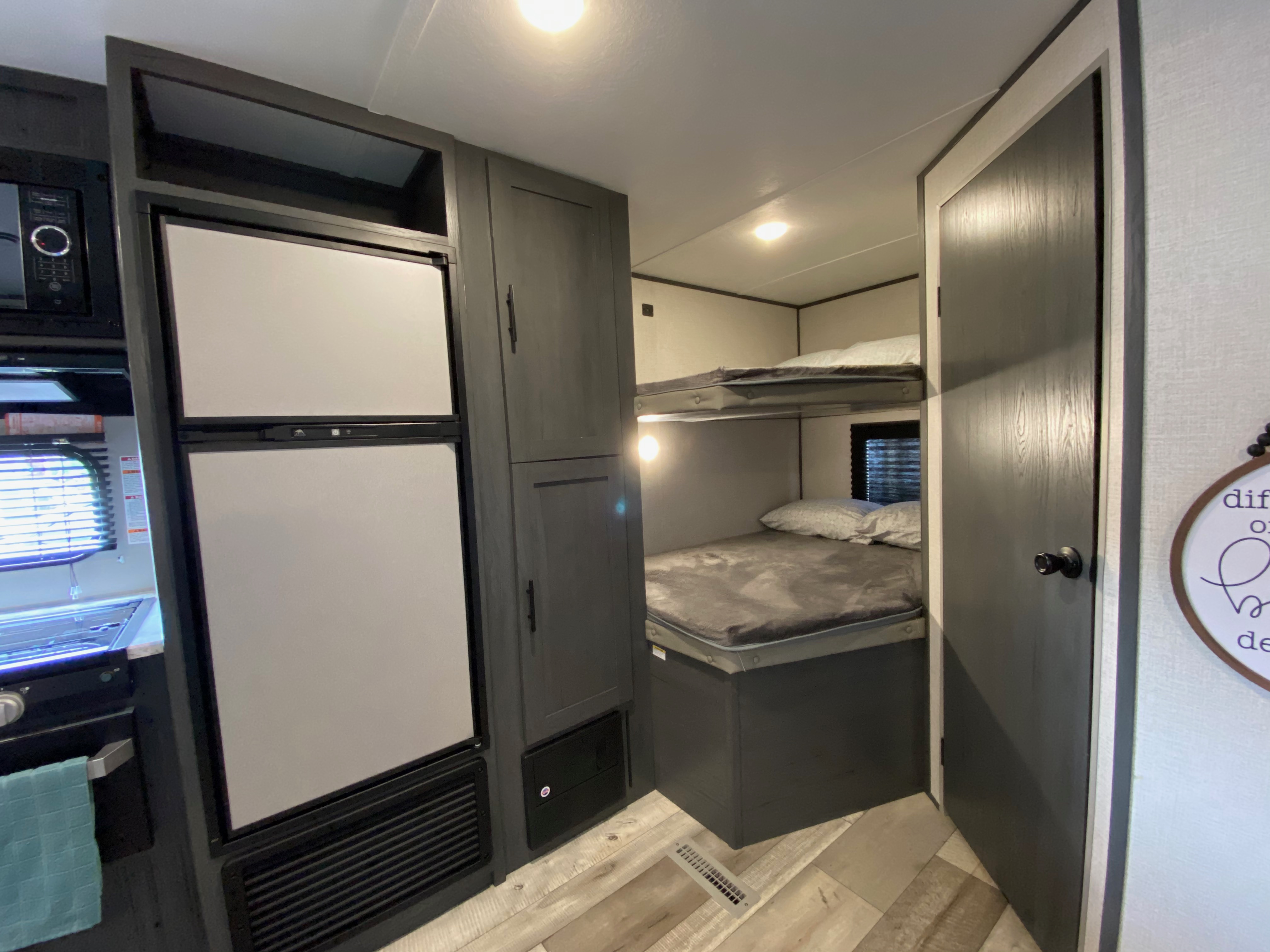 This RV rental interior features a compact kitchen with a large fridge, microwave, stove, dark grey cabinets, and bunk beds.. Dutchmen Aspen Trail 2021
