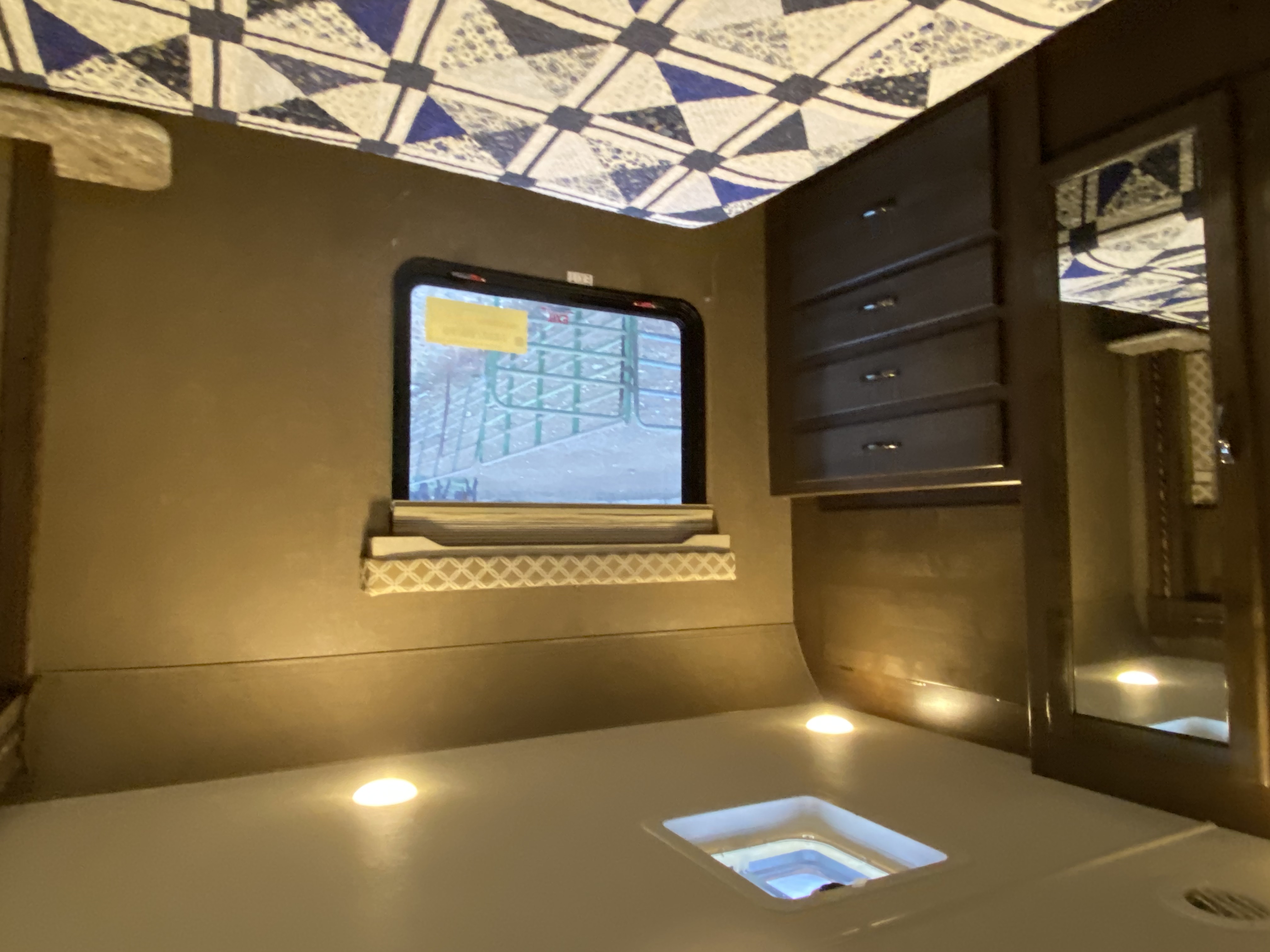 Inside an RV rental: a cozy interior with a patterned ceiling, window, wood cabinet, mirror, and illuminated floor with a drain.. Thor Freedom Elite 2018