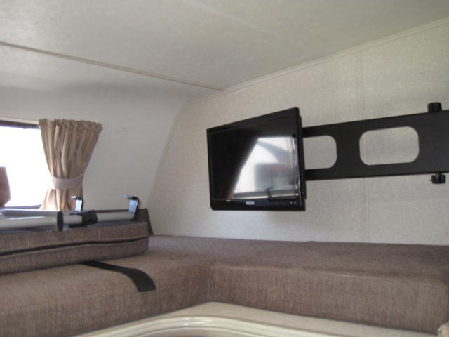 RV rental interior: small TV on a robust swing-arm mount, overlooking a cushioned bunk/seating area.. Coachmen Leprechaun 2019