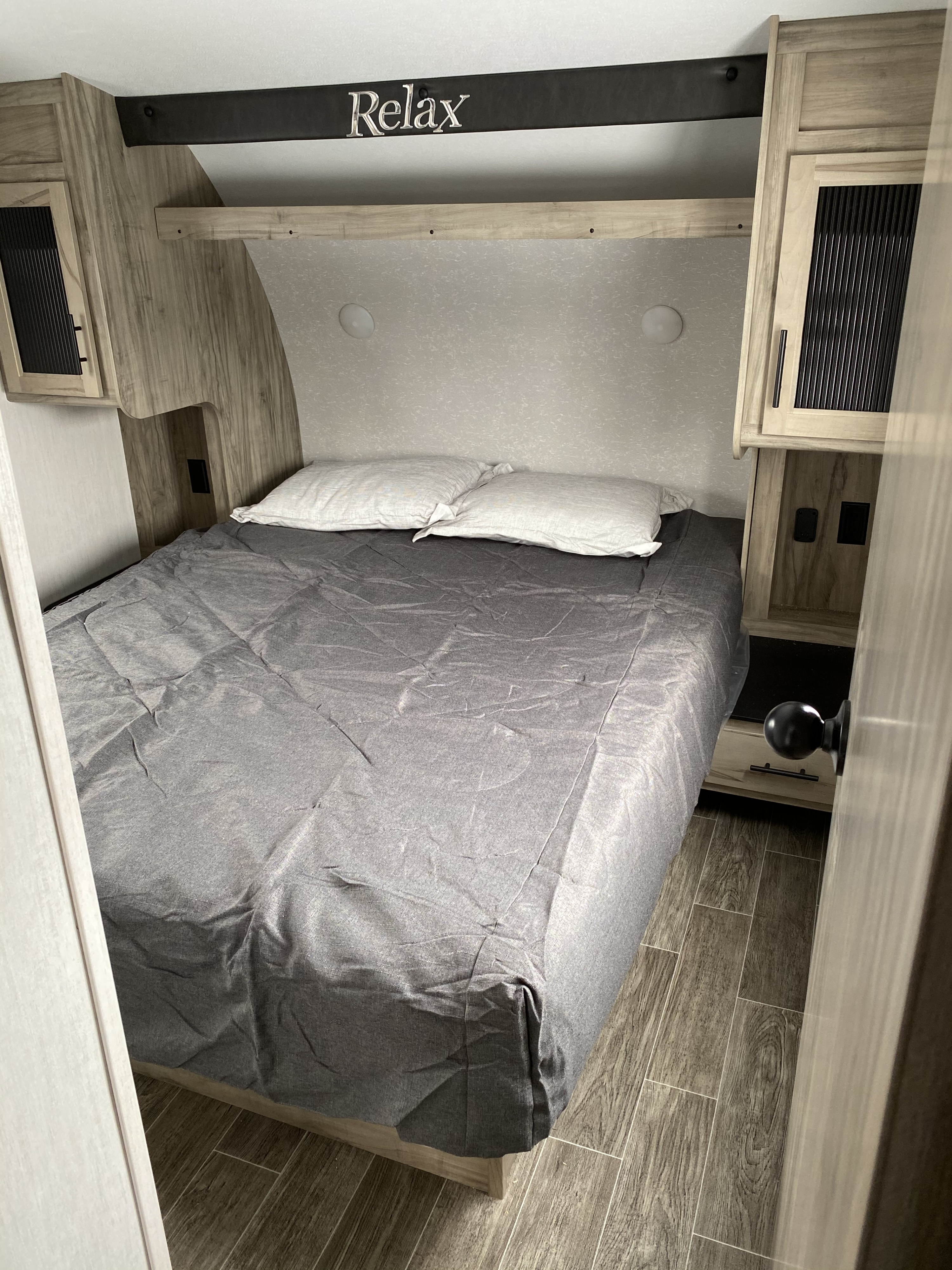 Cozy RV rental bedroom with gray bedding, built-in storage, and a "Relax" sign, offering a comfortable sleeping area.. Forest River Artic Wolf 2021