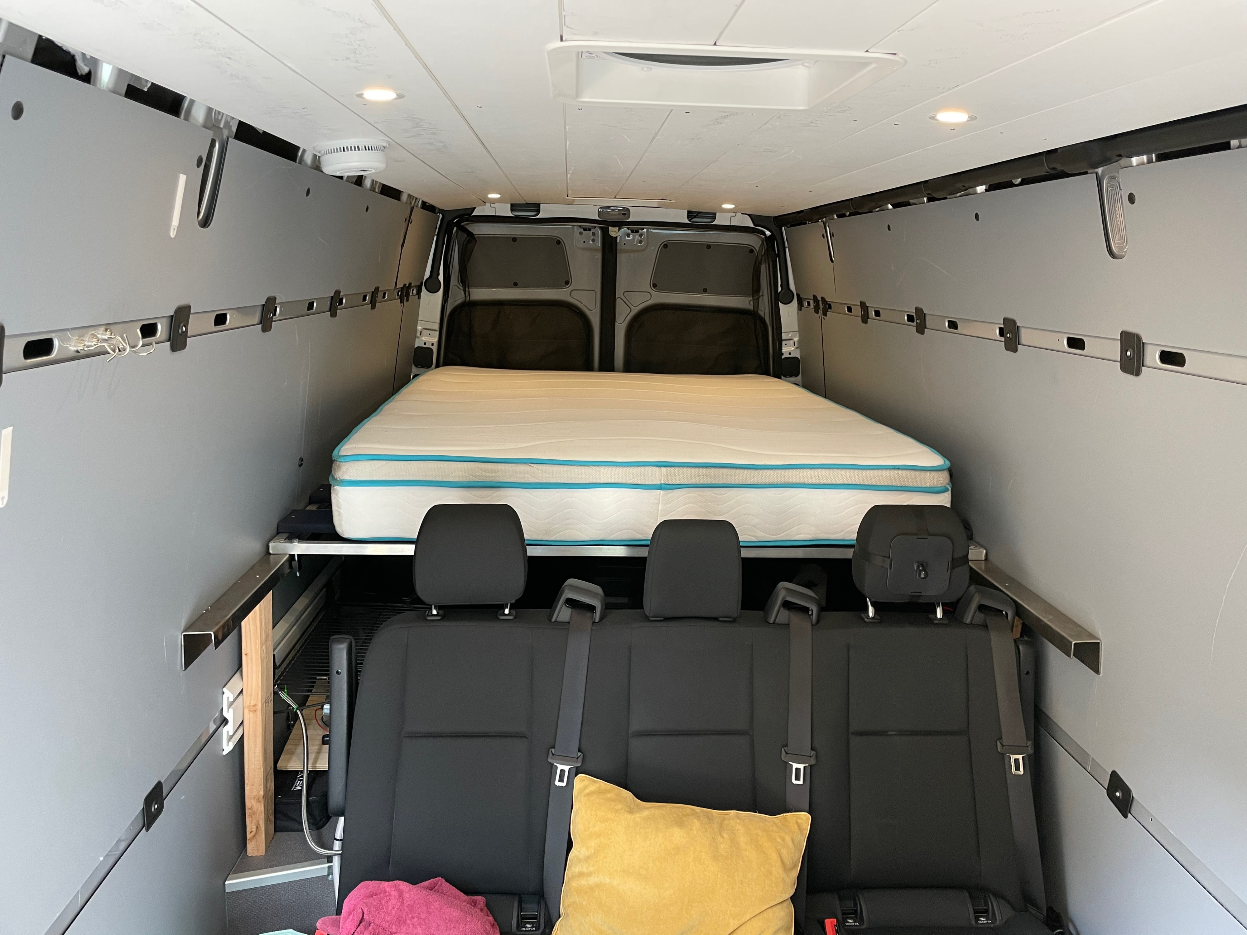 Interior of an RV rental showing a comfy bed and passenger seats in a custom camper van conversion, ready for travel.. Other Sprinter 2019
