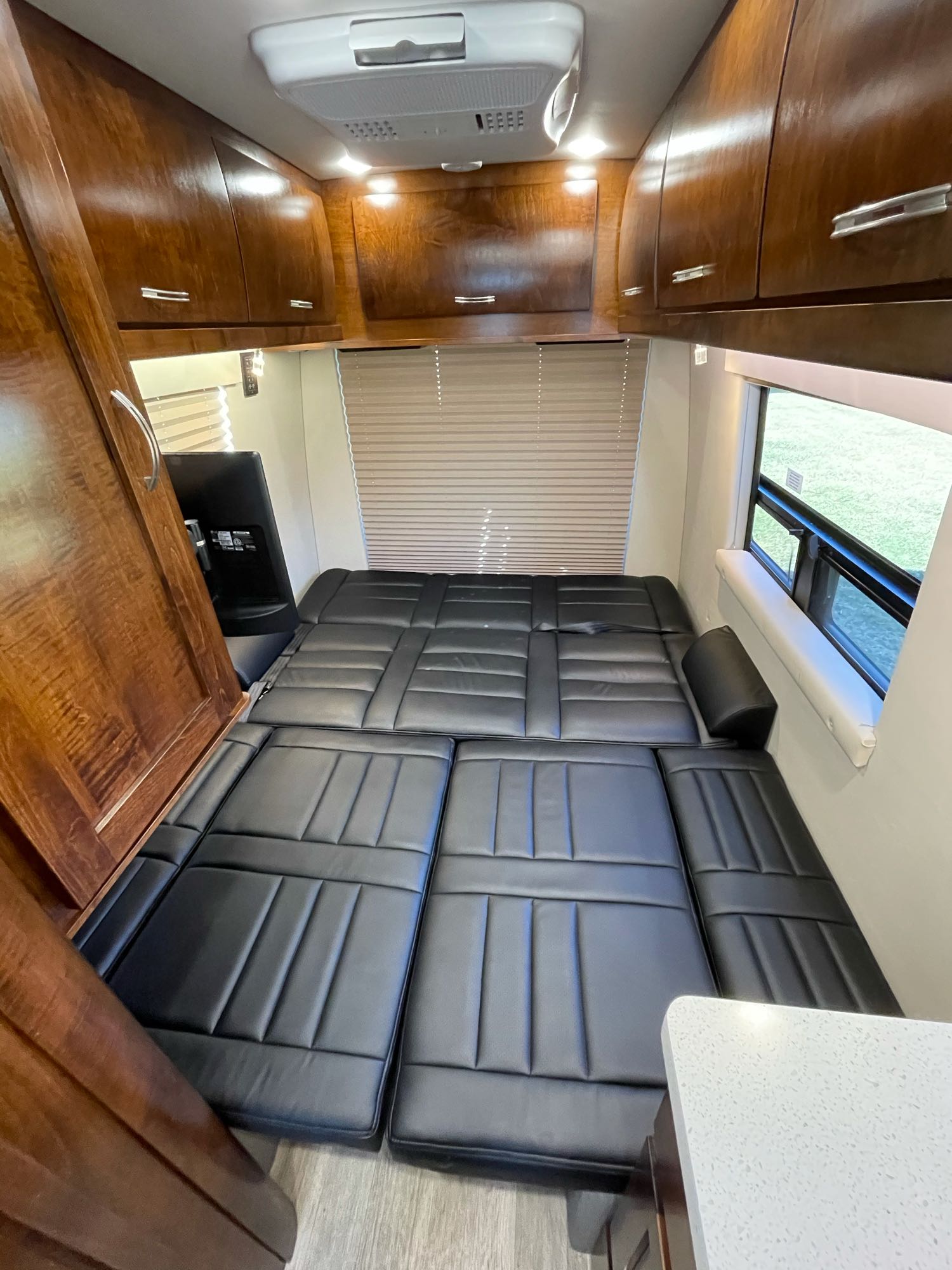 Inside this RV rental: a flexible black cushioned bed, overhead wood cabinets, and a window view. Ideal for compact living.. Coachmen Galleria 24Q 2018