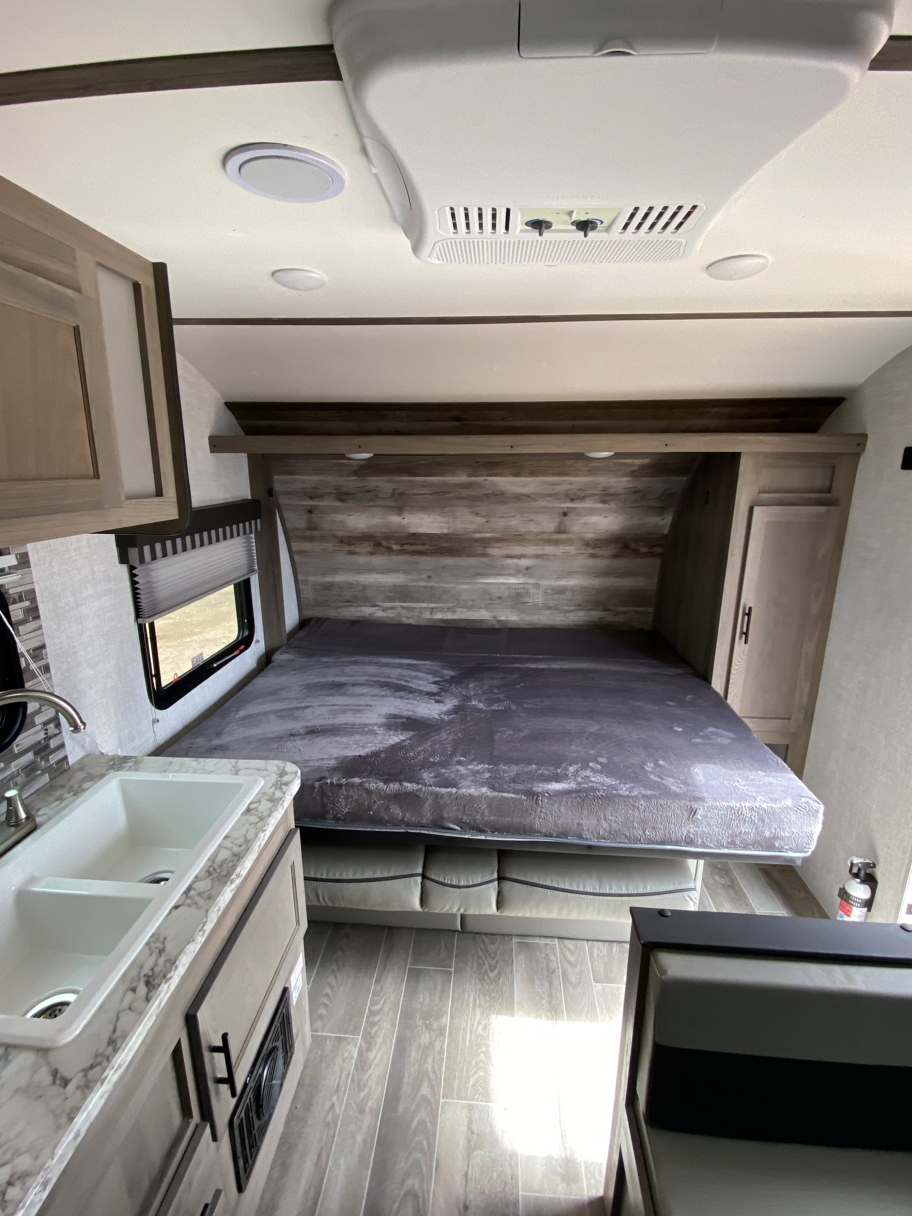 RV rental interior features a gray bed, wood-look wall, kitchen sink area, and overhead AC unit for comfort.. Gulf Stream Conquest Ultra 2021
