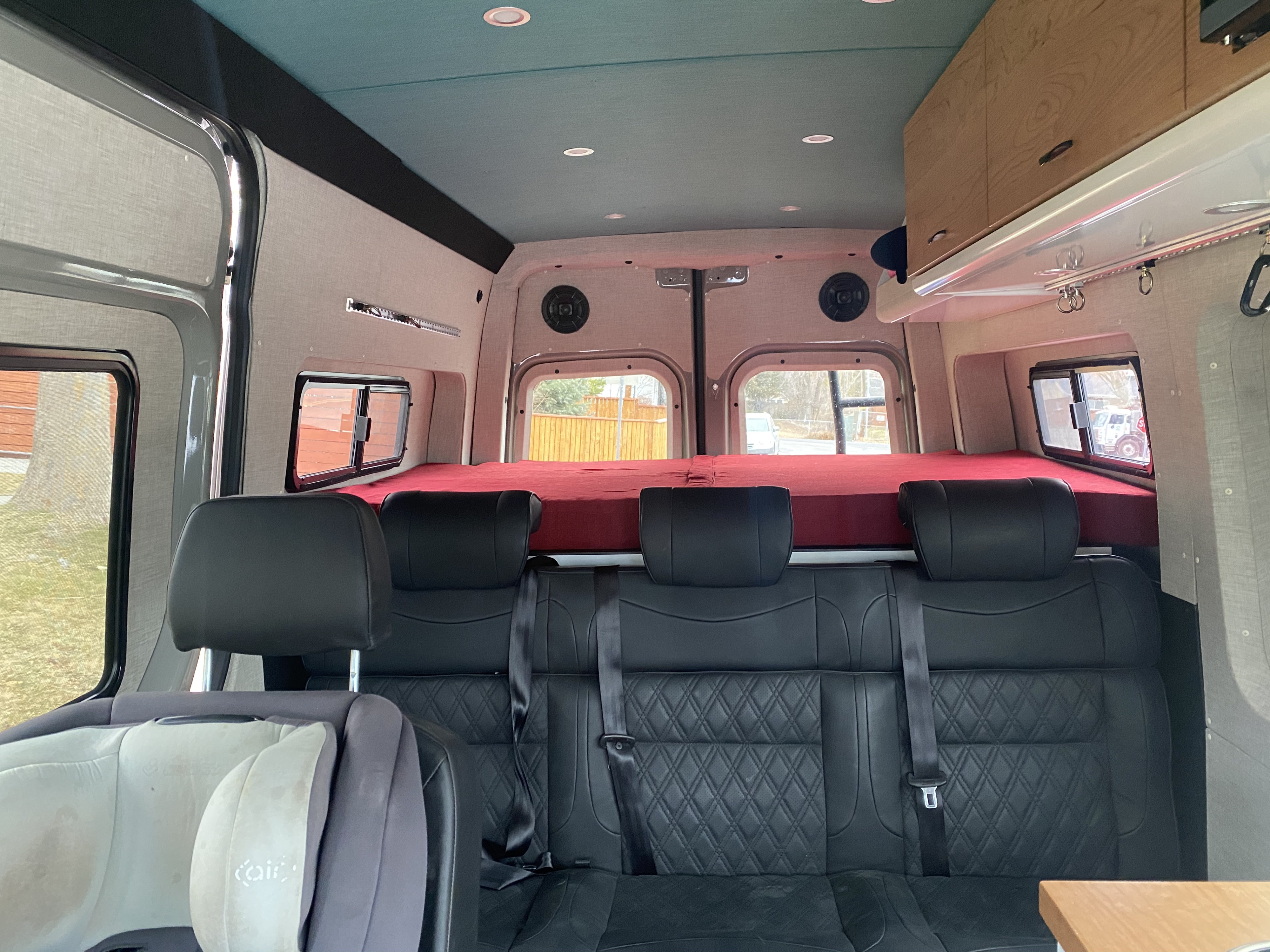 View of an RV rental interior: three quilted seats, raised red bed, teal ceiling, and custom cabinets. Ready for travel.. Mercedes-Benz Sprinter 2020