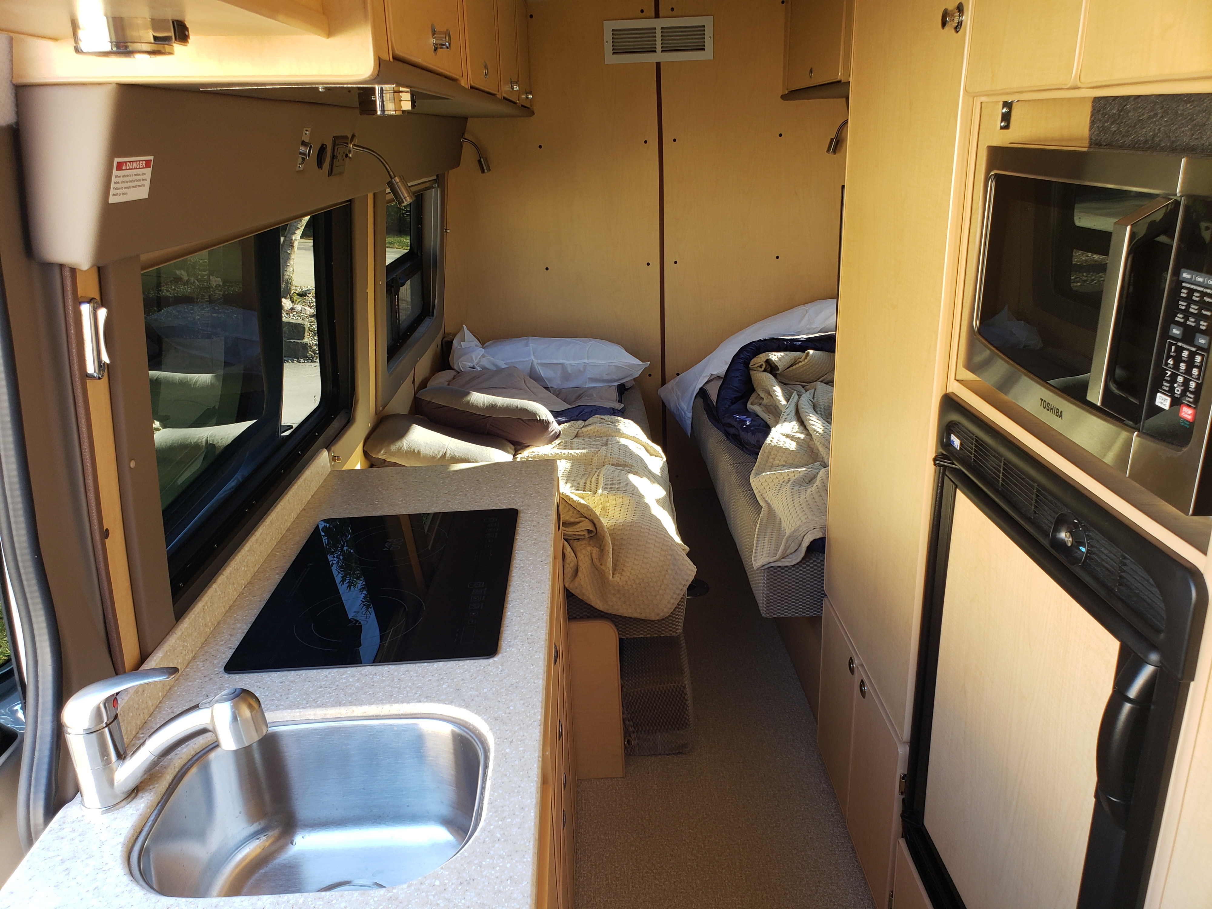 Compact RV rental interior featuring a kitchenette, twin beds, microwave, and fridge, perfect for travel adventures.. Mercedes SPRINTER 313 CDI HIGH ROOF MOTORHOME 2020