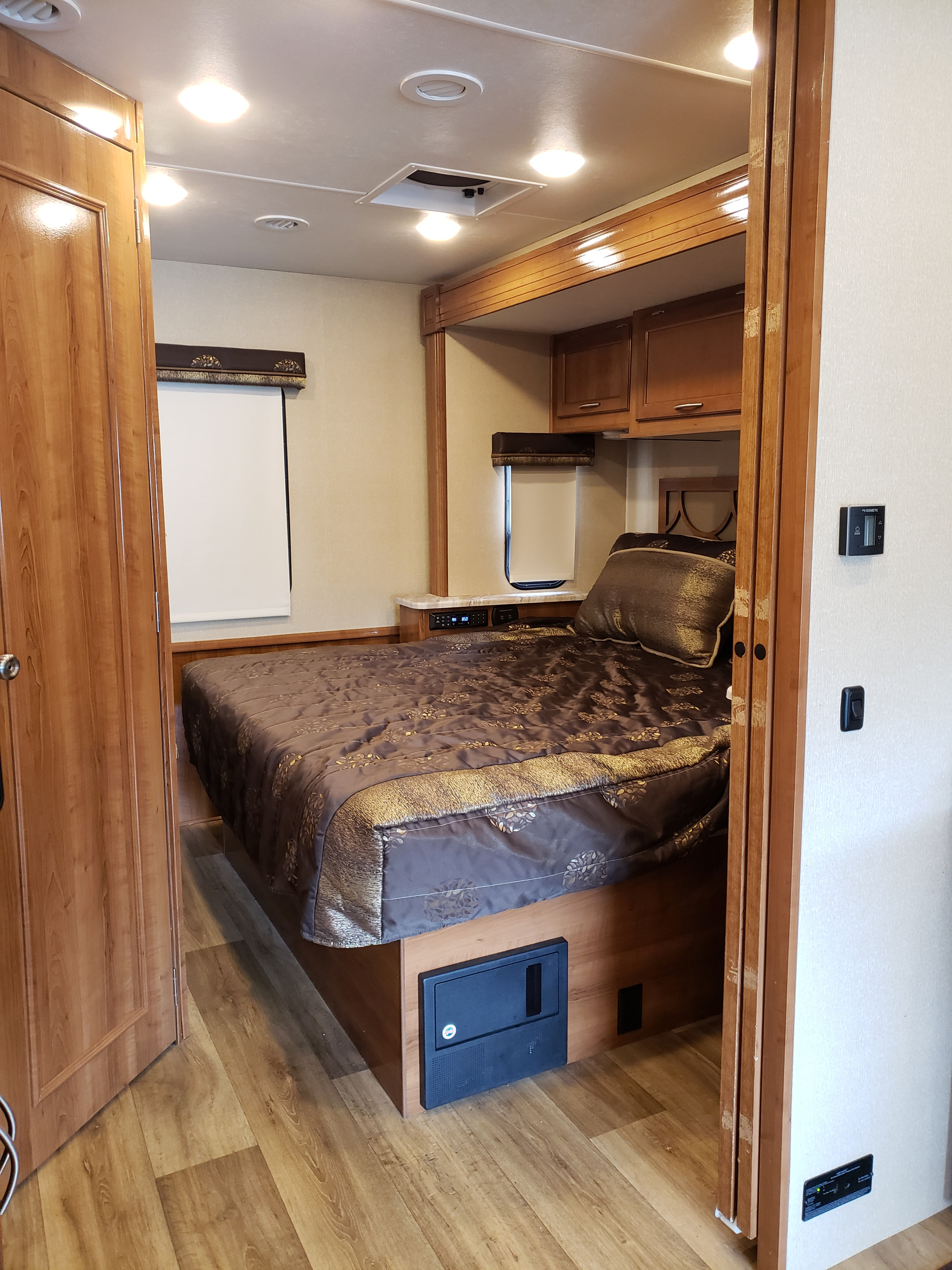 Compact rv rental bedroom featuring a large bed with ornate bedding, wood cabinetry, and controls.. Coachmen Pursuit Precision 27 DSP 2018