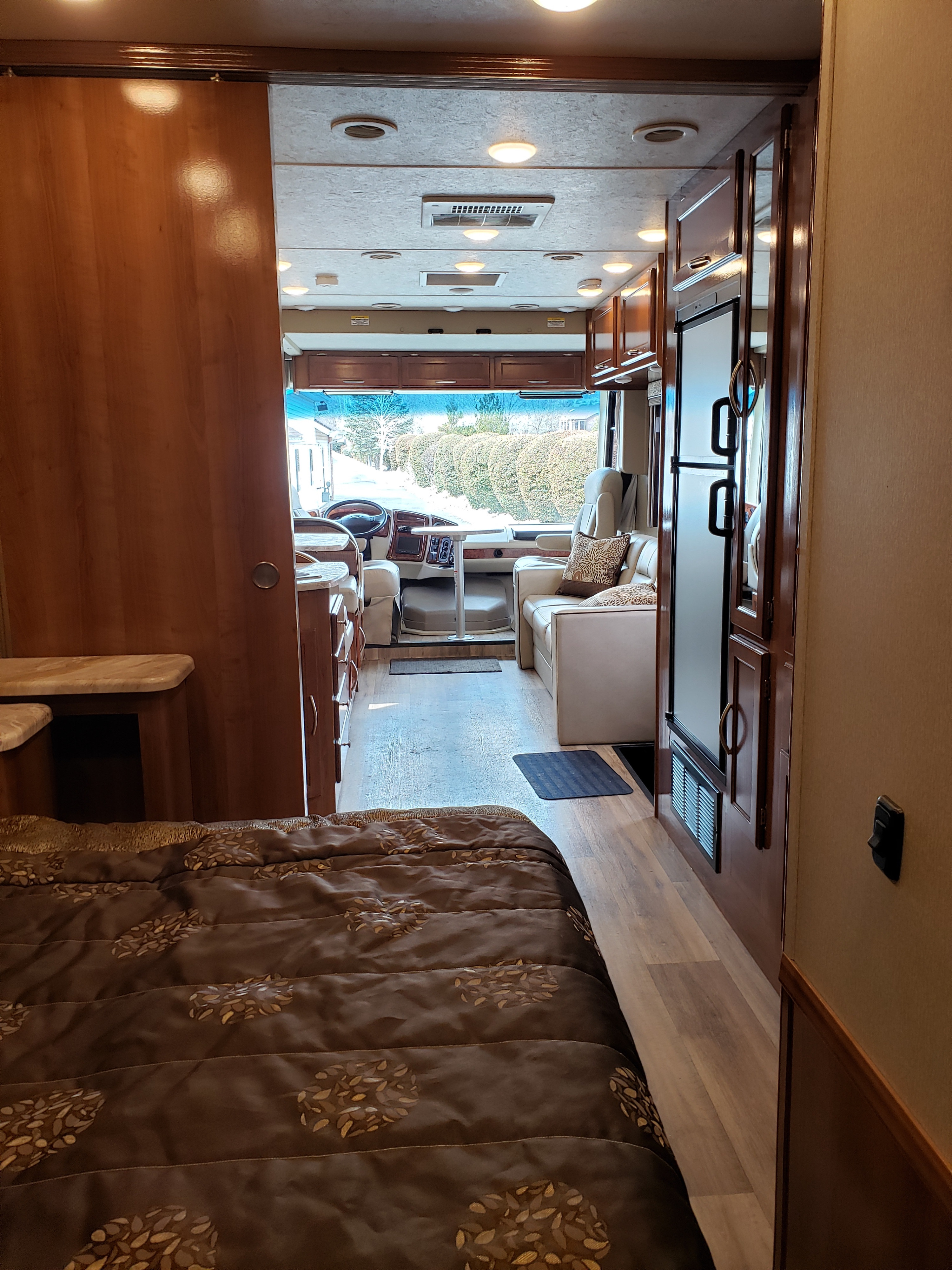 Inside a comfortable RV rental: the view stretches from the patterned bed, past an open wooden door, to the inviting living area & cabin.. Coachmen Pursuit Precision 27 DSP 2018