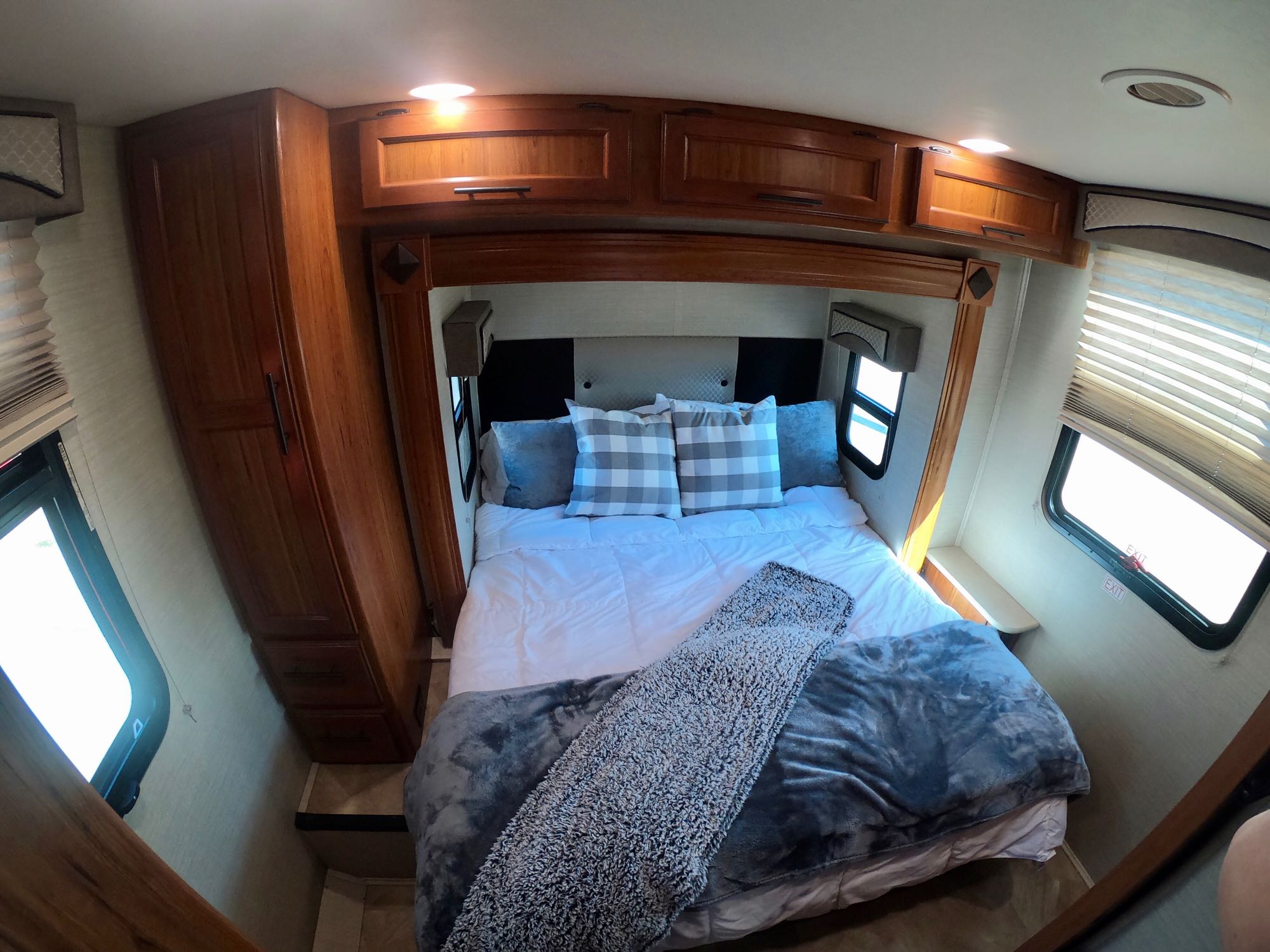 Inside a cozy RV rental bedroom, featuring a comfy bed with soft blankets, plaid pillows, wooden cabinets, and bright windows.. Jayco Melbourne 2017