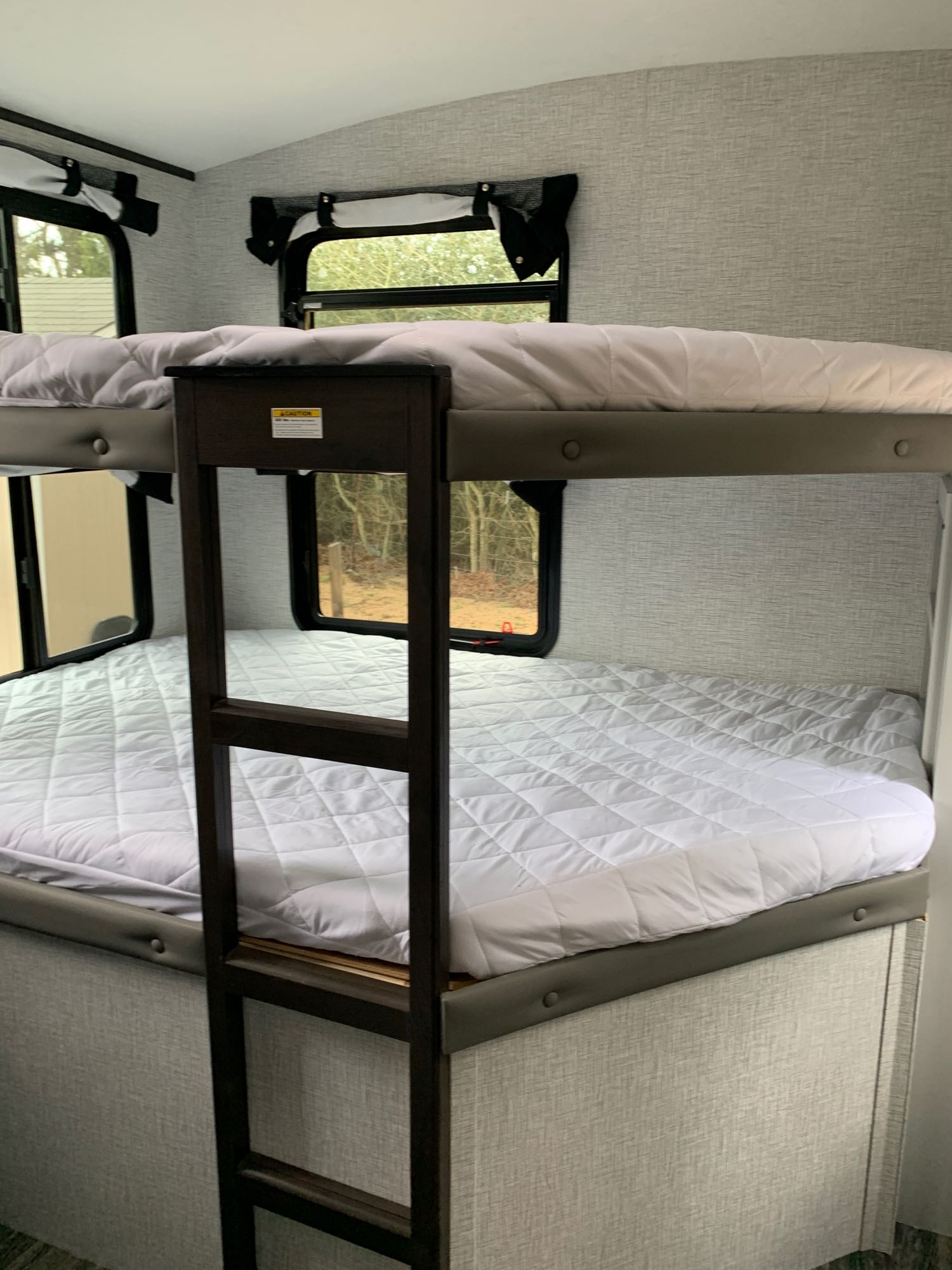 Cozy RV rental bunk beds with white quilted mattresses, a sturdy ladder, and windows showcasing outdoor views.. Keystone RV Bullet Ultra Lite 2021