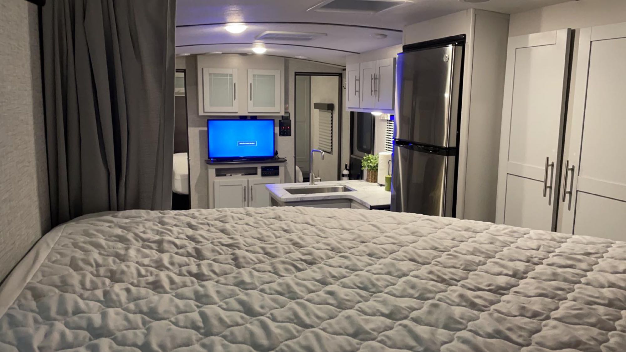 Step inside this RV rental: a cozy bed, compact kitchen with sink and TV, plus a full-size fridge. Modern interior.. Keystone RV Bullet Ultra Lite 2021