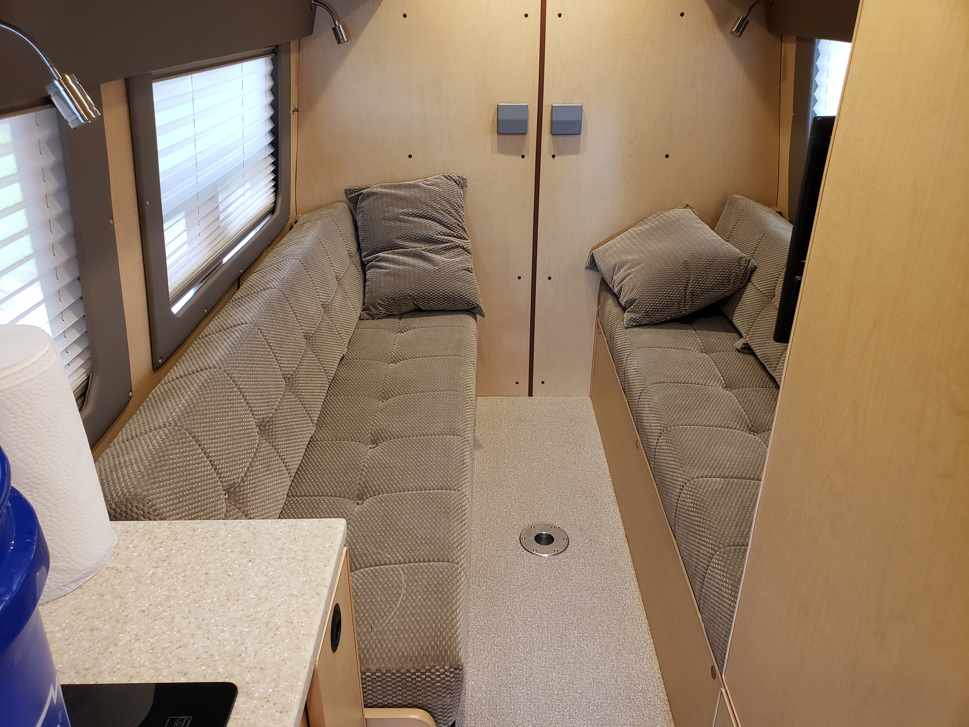 Cozy RV rental interior with facing upholstered benches, wood walls, windows, and functional design for compact living.. Mercedes SPRINTER 313 CDI HIGH ROOF MOTORHOME 2020