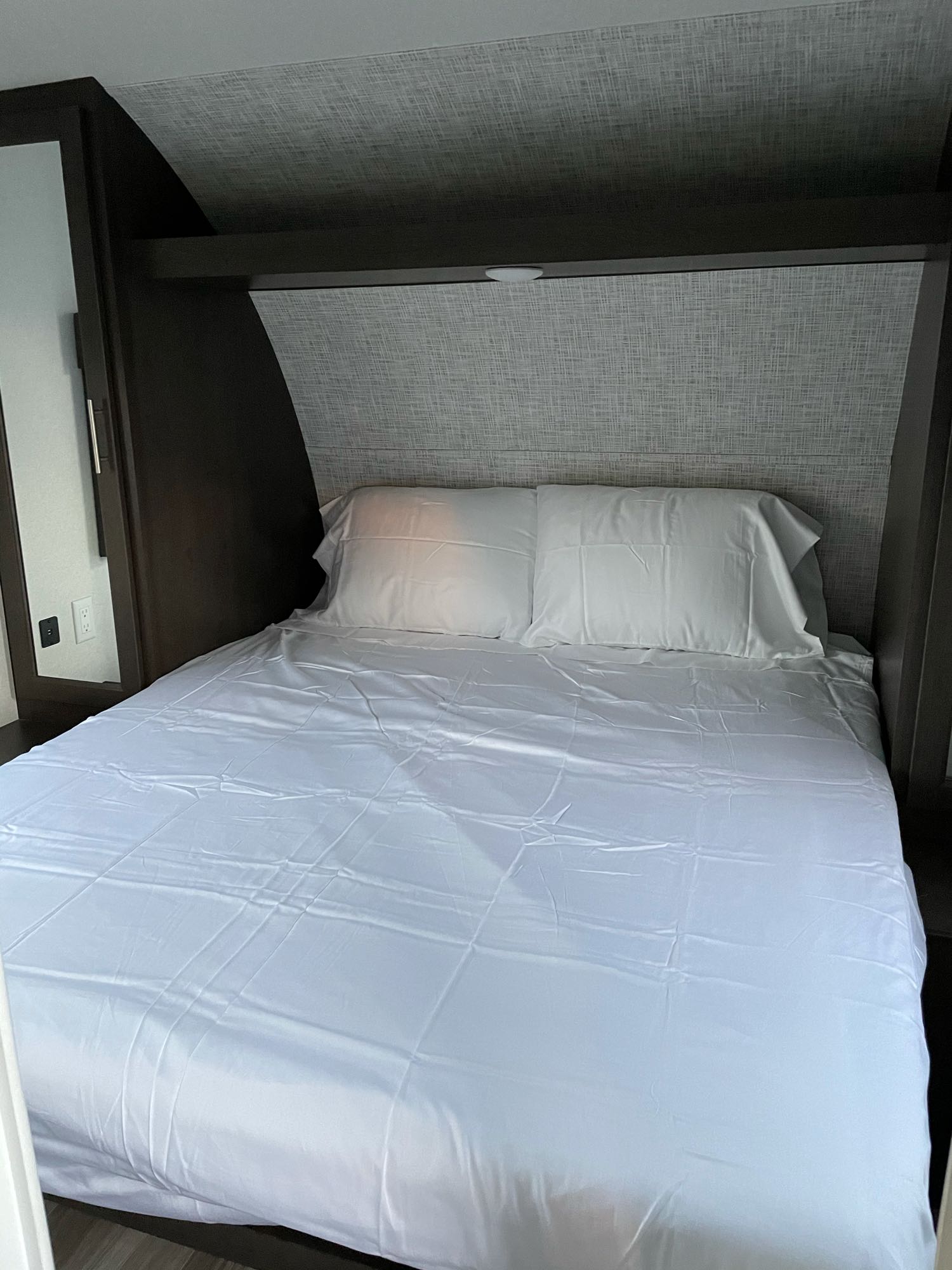 Comfortable RV rental bed with crisp white linens and convenient overhead storage in a compact bedroom.. Forest River Cruise Lite 2020