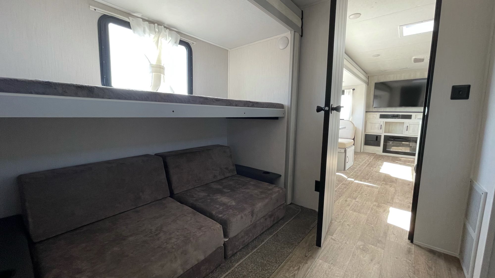 Modern RV rental interior showing a bunk bed over convertible seating and a view into the living room with a TV.. Forest River Vibe 2021