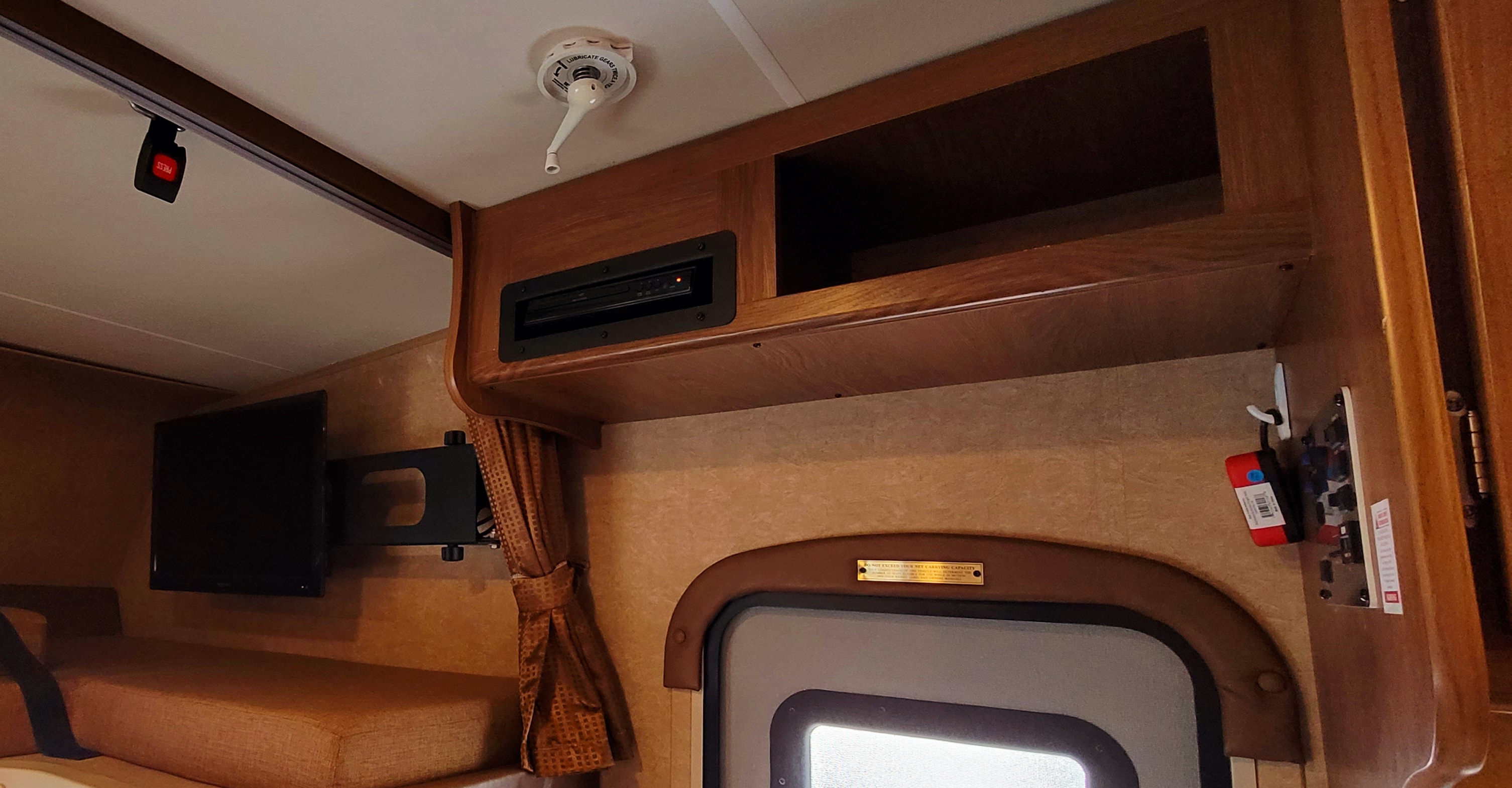 RV rental interior: bunk bed with TV, wooden cabinets, entertainment unit, and a ceiling crank for pop-top/awning. Controls nearby.. Coachmen Leprechaun 2016