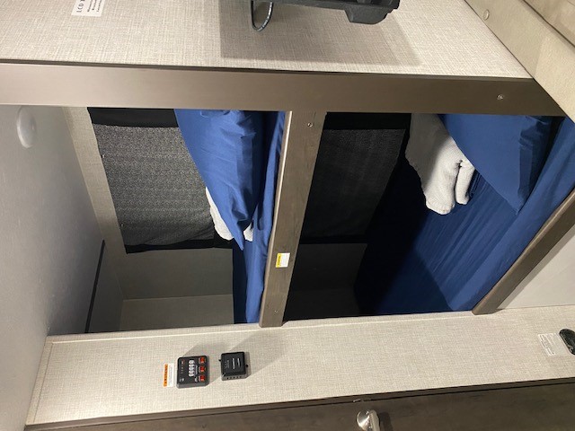 RV rental bunk beds: a compact sleeping area with blue bedding, mesh safety netting, and wall-mounted control panels.. Keystone Bullet 2021