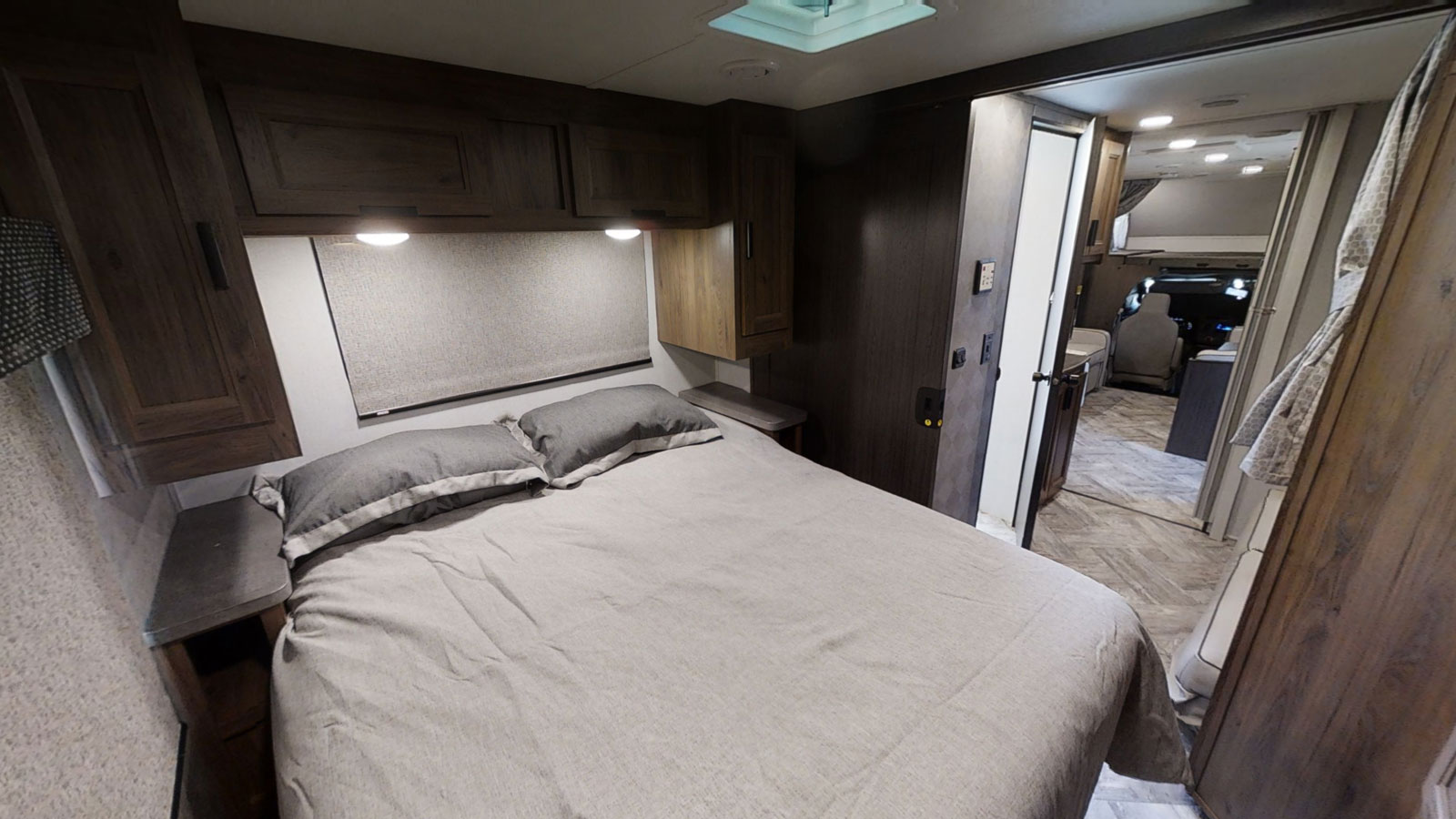 Cozy RV rental bedroom interior with a comfortable bed, overhead cabinets, and soft lighting, looking towards the front cab.. Forest River Forester 2018