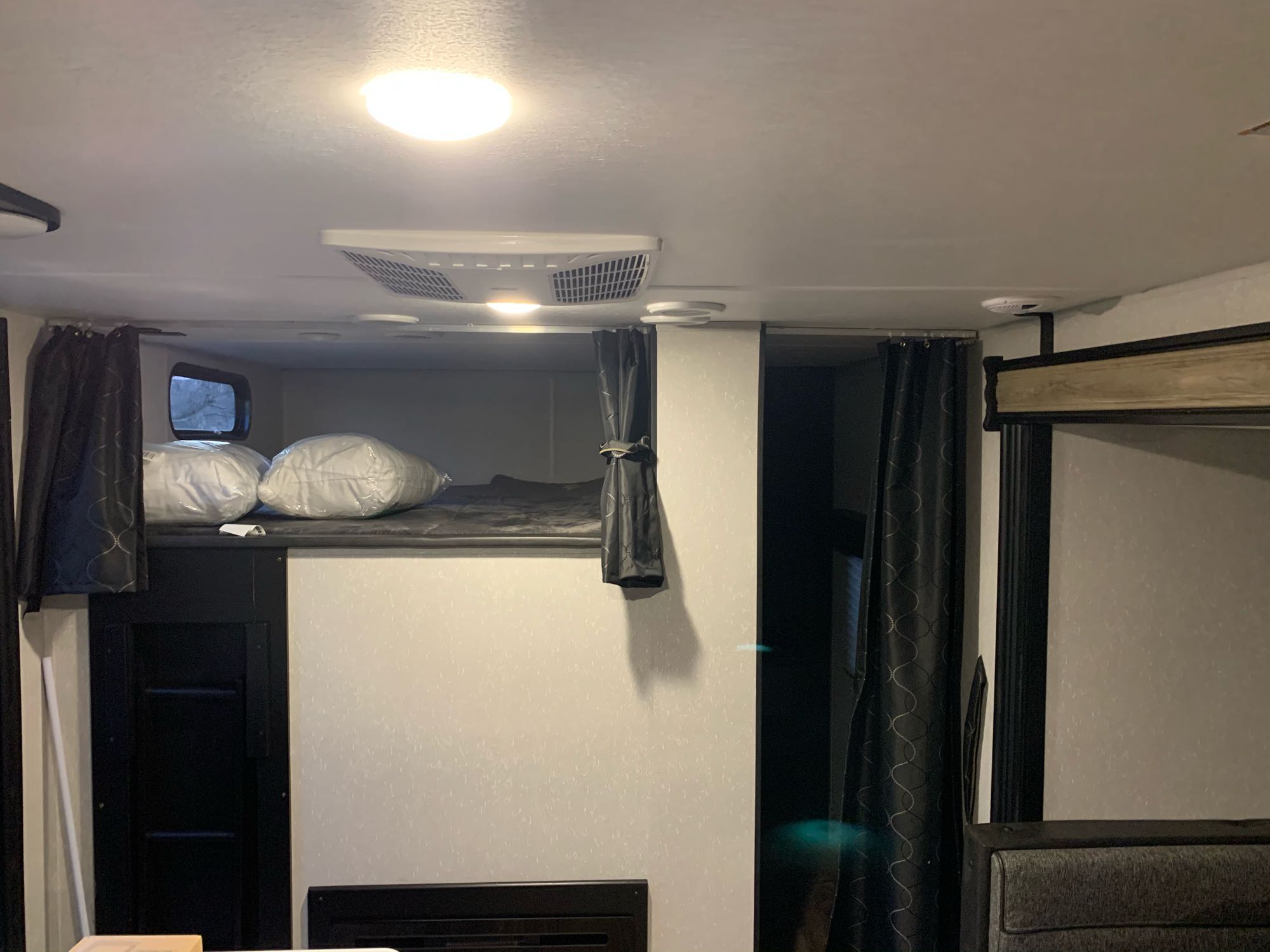 Inside an RV rental, showing a cozy bunk bed area with pillows, dark curtains, and an overhead AC unit.. Forest River Cherokee 2021