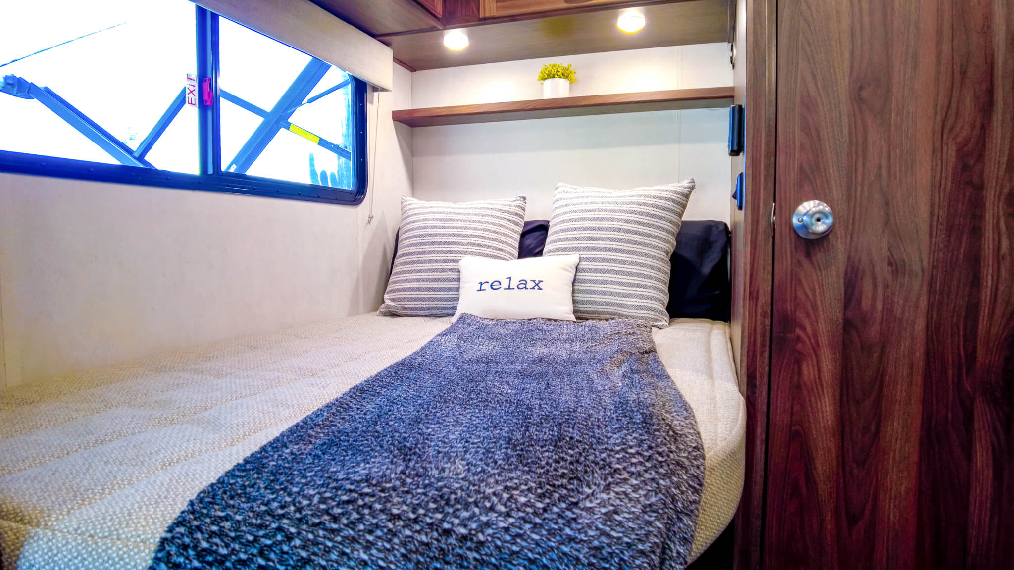 Bright RV rental bedroom: cozy bed with "relax" pillow, window, and wooden cabinets.. Winnebago Vita 2020