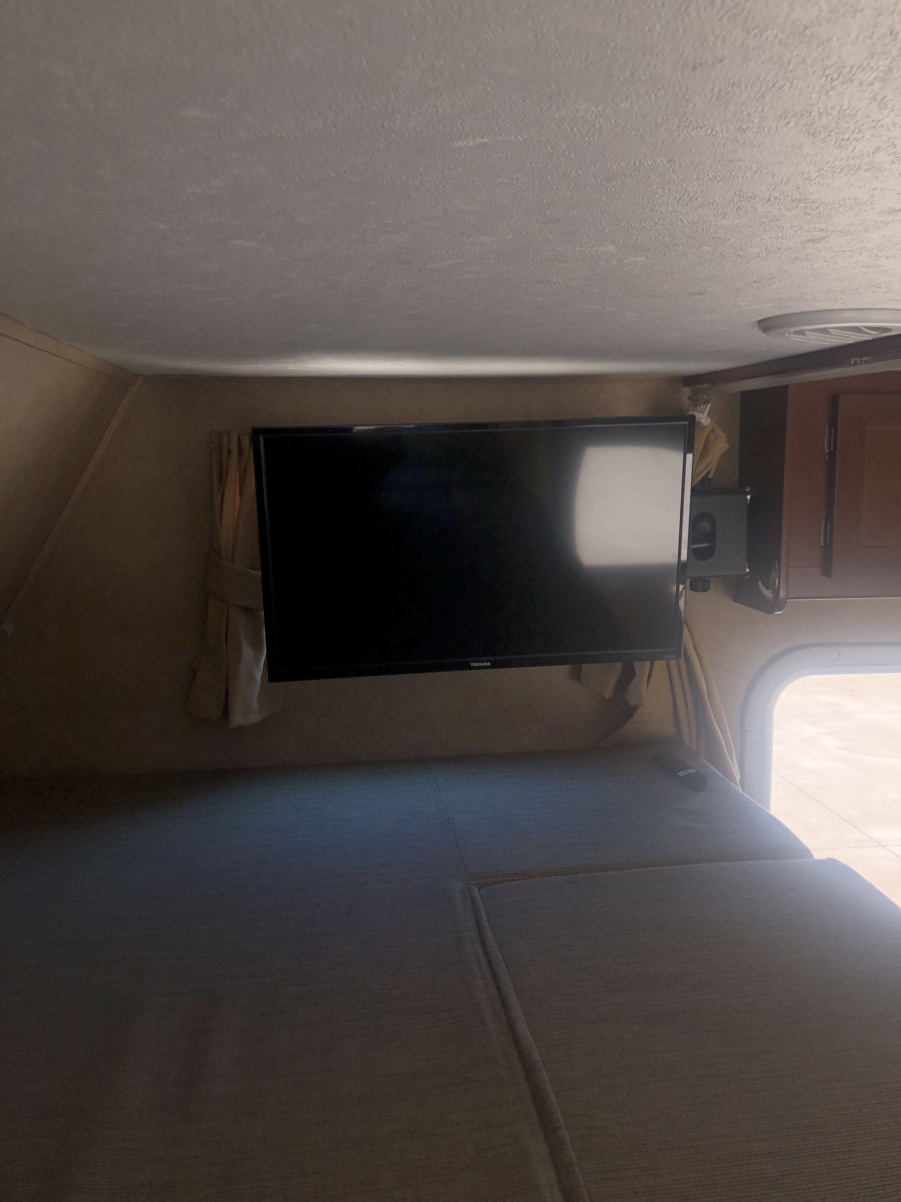 Inside an RV rental: a cozy overhead bed with a mounted Toshiba TV and window, offering a comfortable viewing space.. Forest River Sunseeker 2014