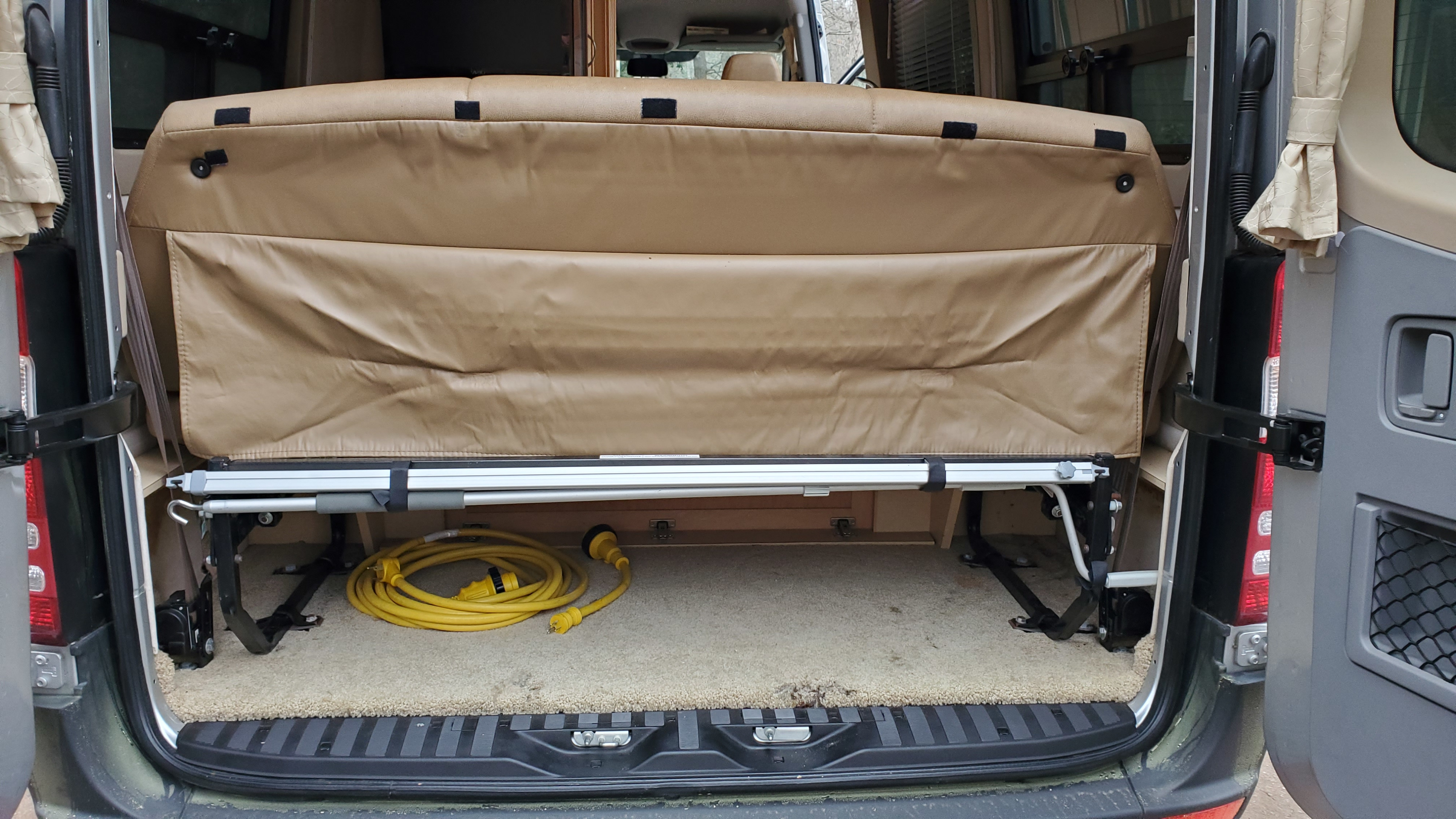 Camper van RV rental: rear interior shows a raised bed, revealing carpeted storage with a yellow power cable.. Pleasure Way Plateau Ts 2013