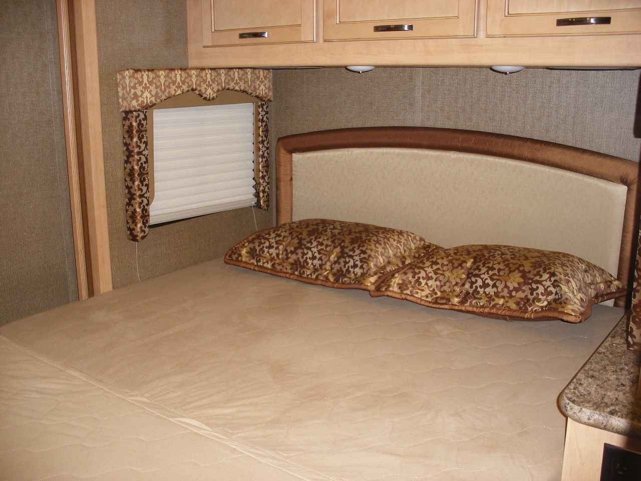 Cozy RV rental bedroom with patterned pillows, window, and overhead cabinets for a comfortable stay on the road.. Thor Motor Coach Freedom Elite 22FE 2017