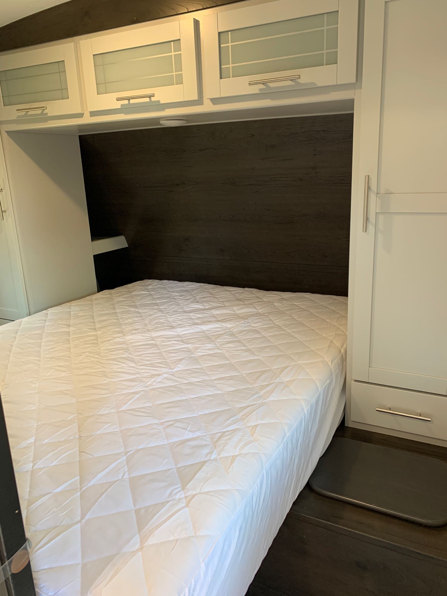 RV rental: Compact bedroom with white quilted bed, sleek dark paneling, and ample overhead storage cabinets.. Keystone RV Bullet Ultra Lite 2021