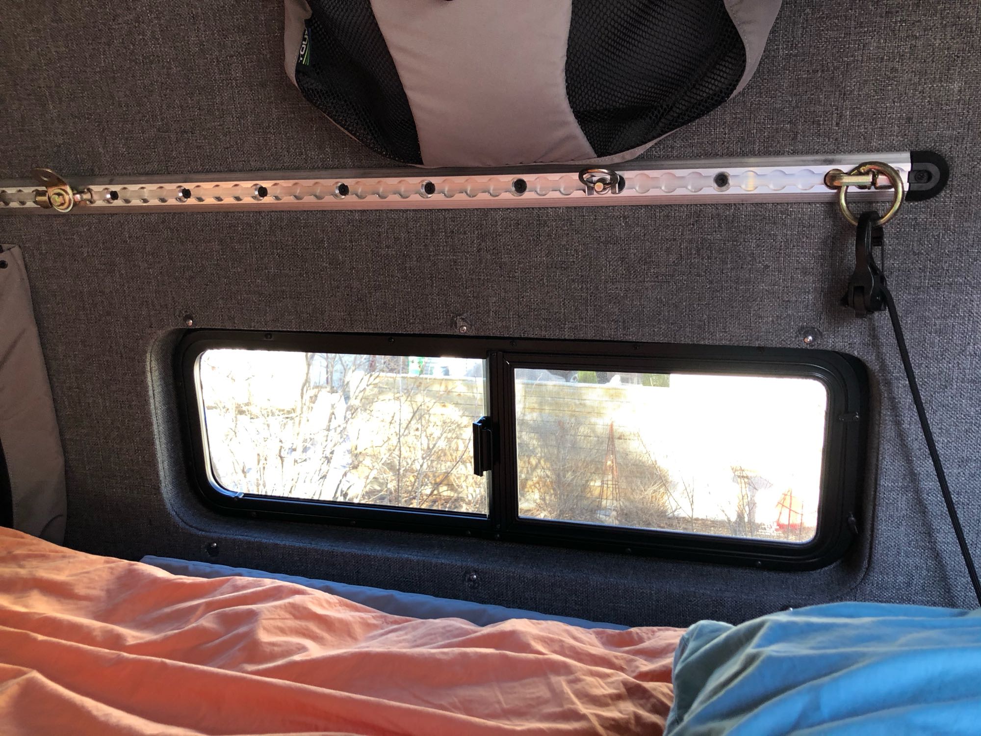 Cozy RV rental interior shows a bed by a window, featuring a versatile L-track system for gear organization.. Mercedes-Benz Sprinter 2014
