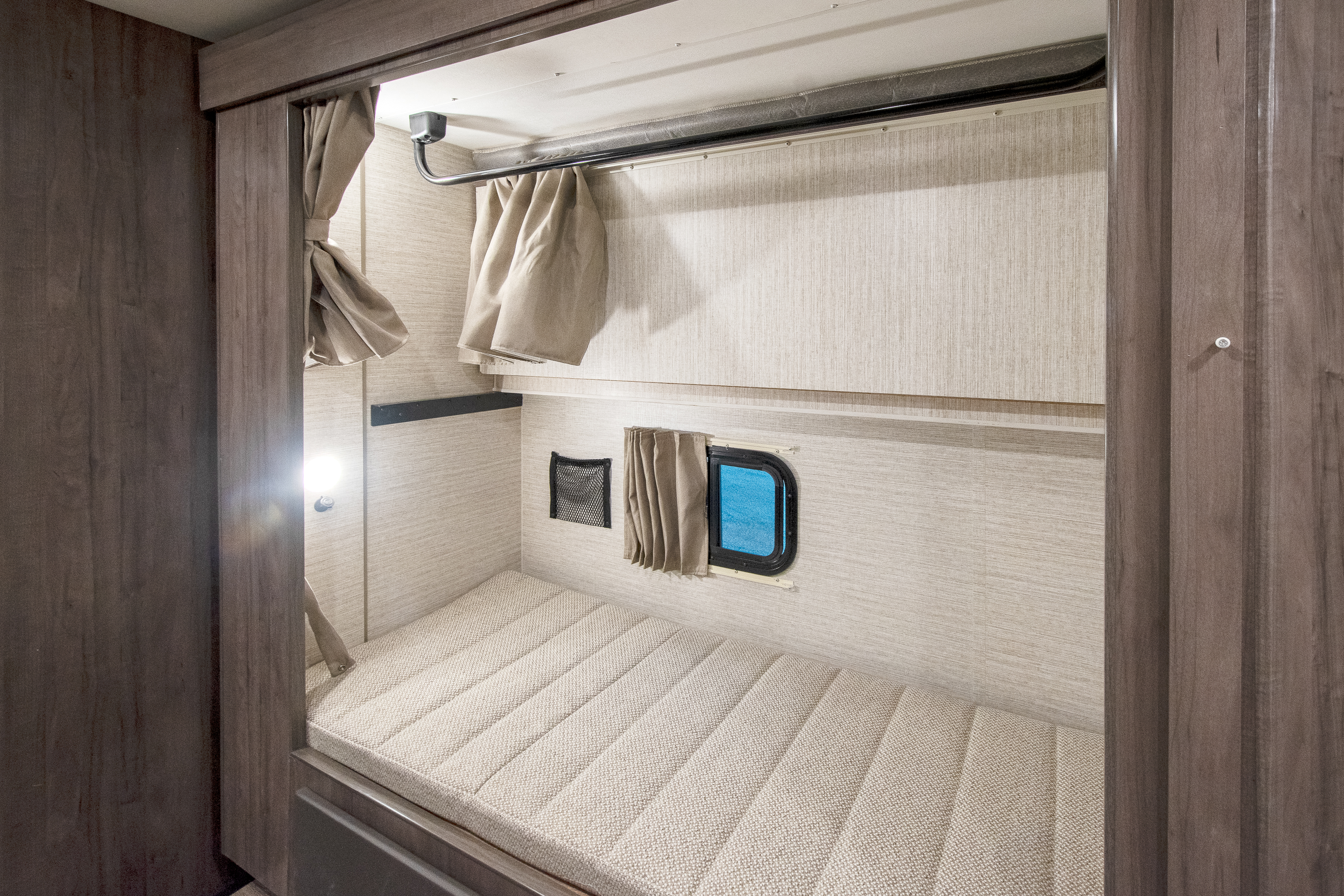 Cozy RV rental bunk beds with privacy curtains. Lower bunk includes mattress, window, light, and storage net.. Winnebago Minnie Winnie 2024