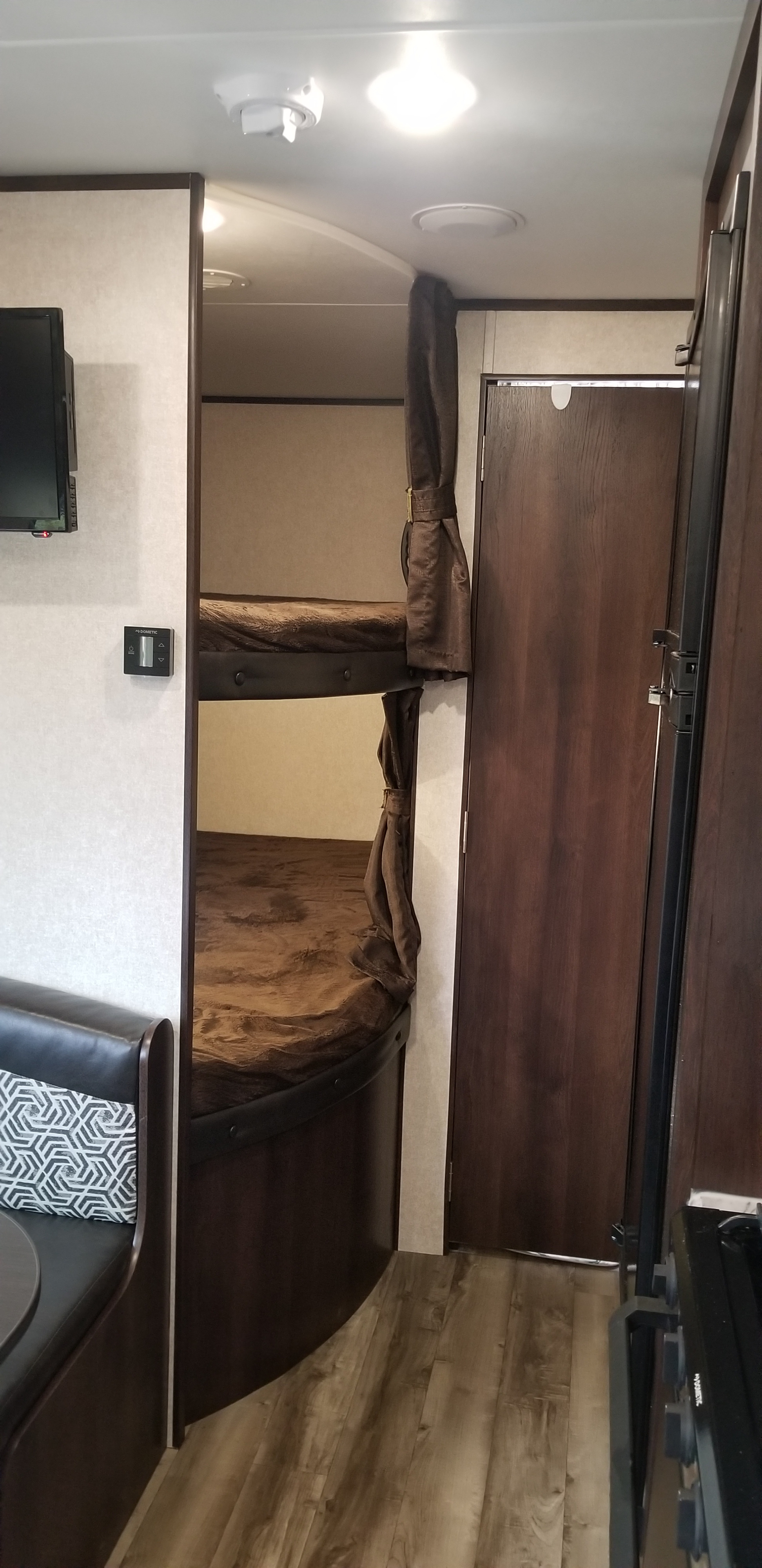 View of an RV rental's sleeping area with bunk beds, adjacent dinette, and TV, offering a compact, functional space.. Jayco Jay Flight 2019
